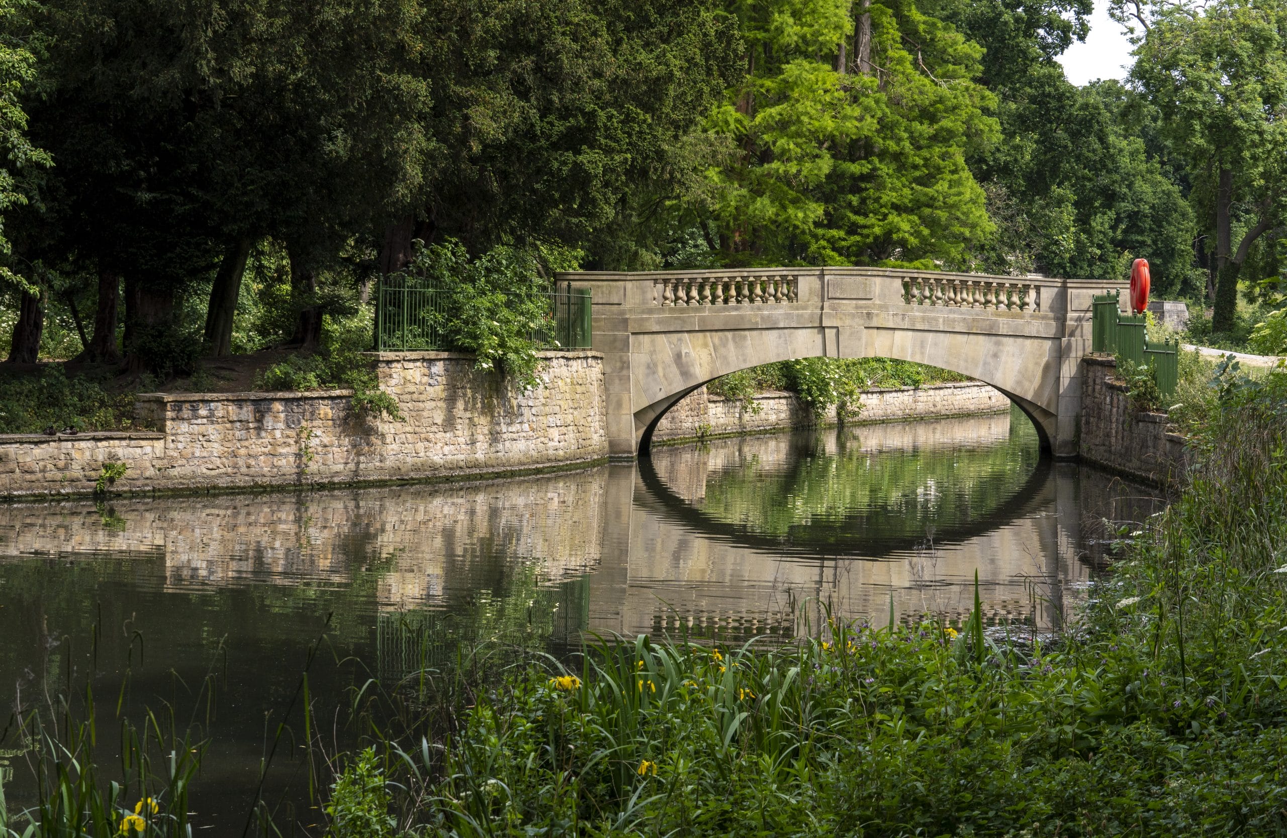 A stone bridge reflected in a lake surrounded by green trees