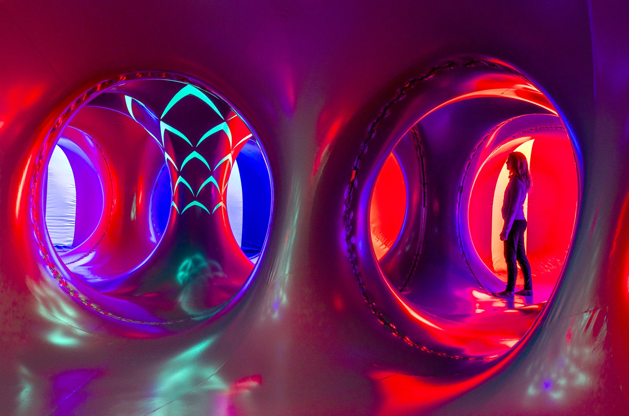 A woman walking through luminarium which is glowing with reds and purples.