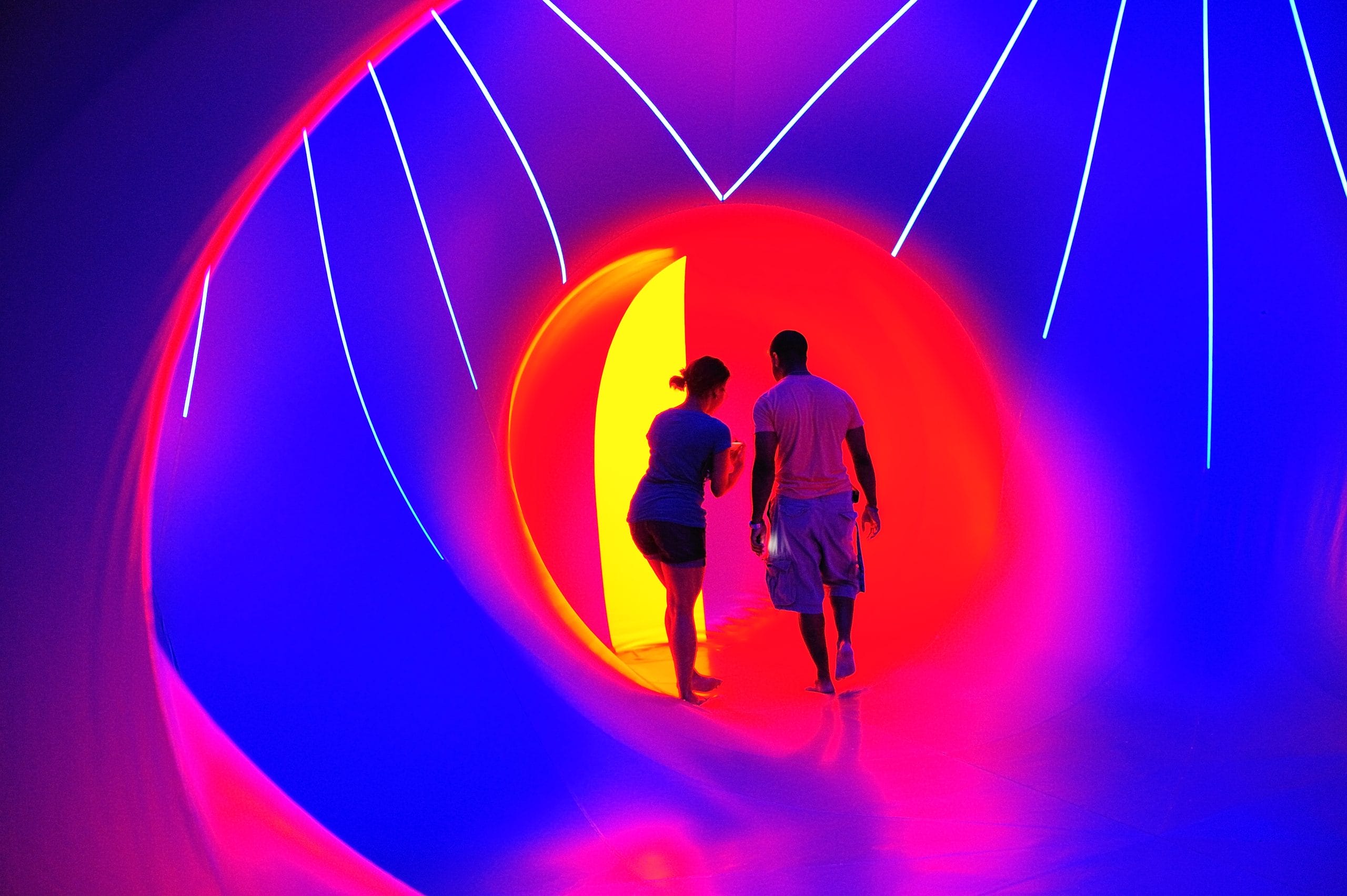 A man and woman looking away from the camera inside a small section of a luminairum, which is glowing red and yellow. They are surrounded by larger blue section with light blue lines.
