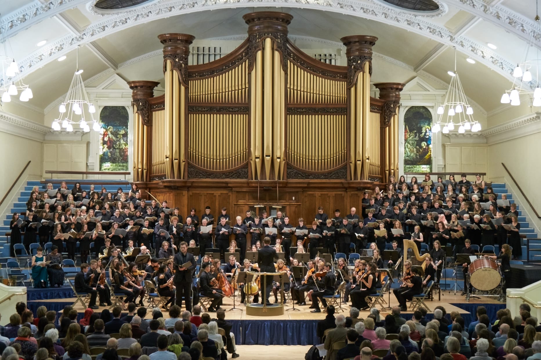 a full orchestra perform in a large space with an imposing organ behind them