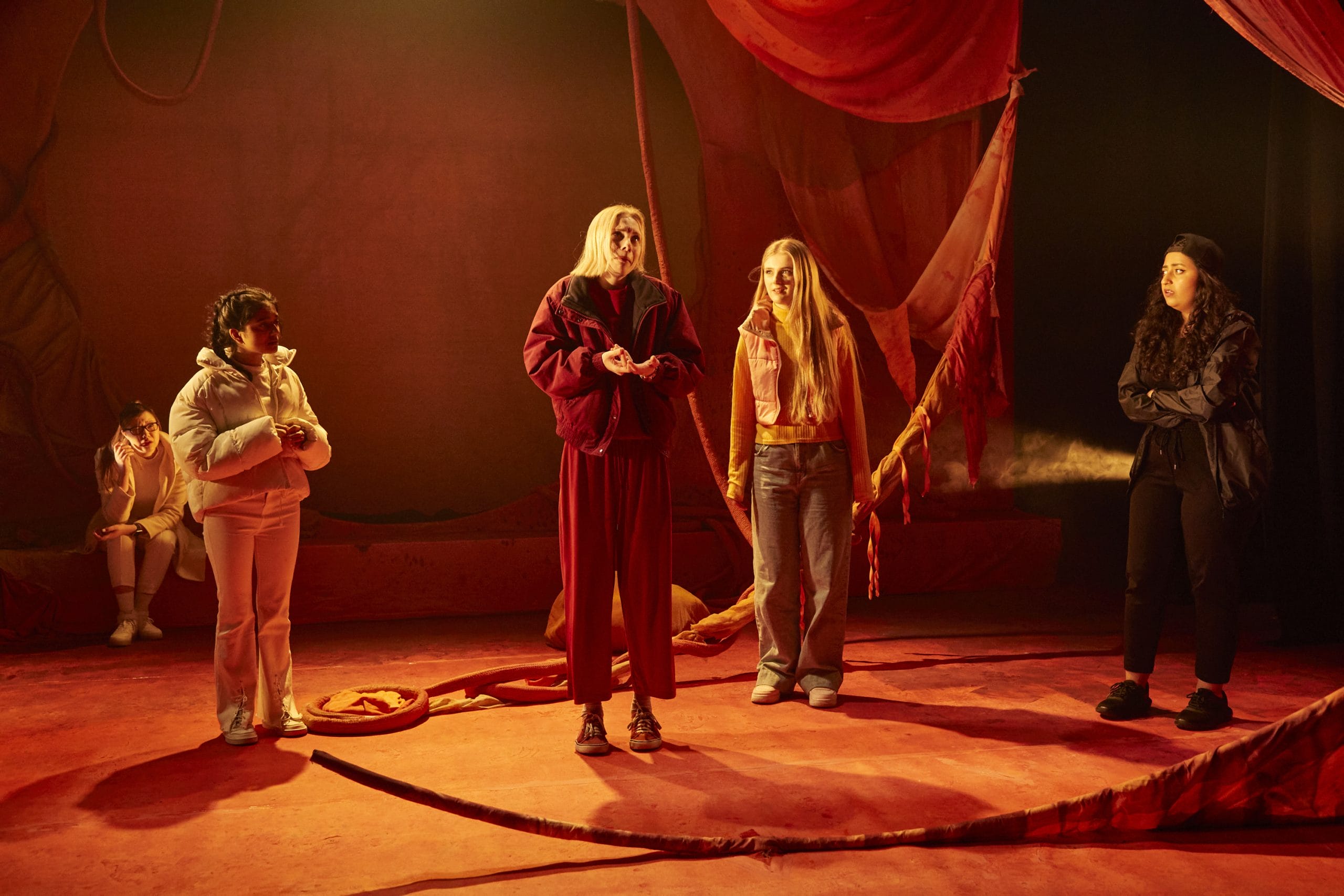four actors stand looking guilty on a red-lit stage