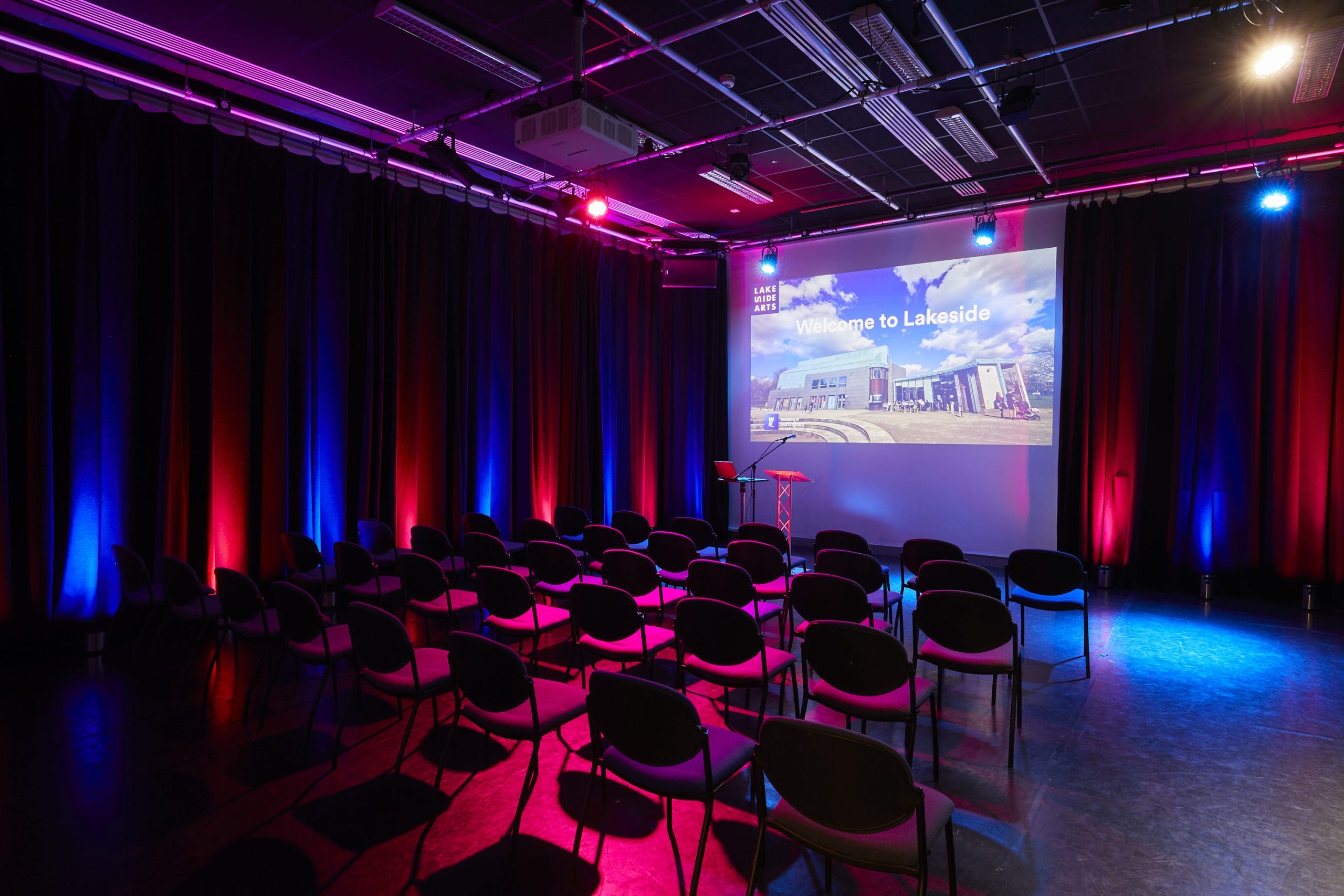 A studio space lit up with red and blue lights. Chair look at a big screen.