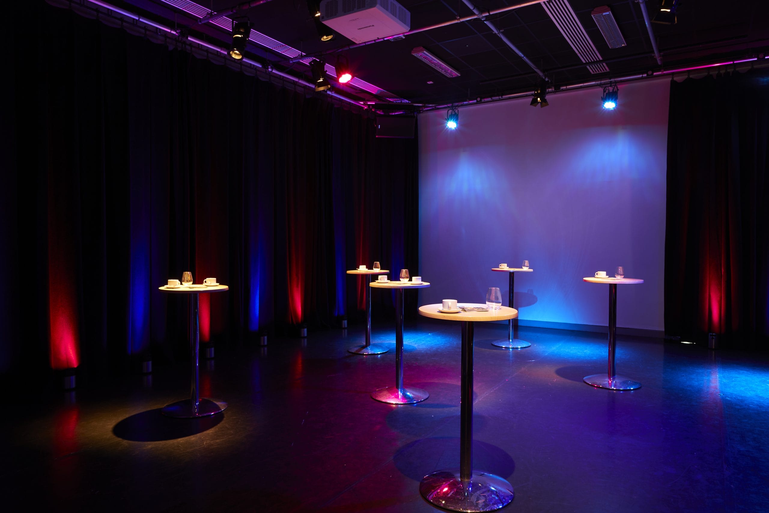 A room lit with red and blue lights set up with high tables with coffee cups on them