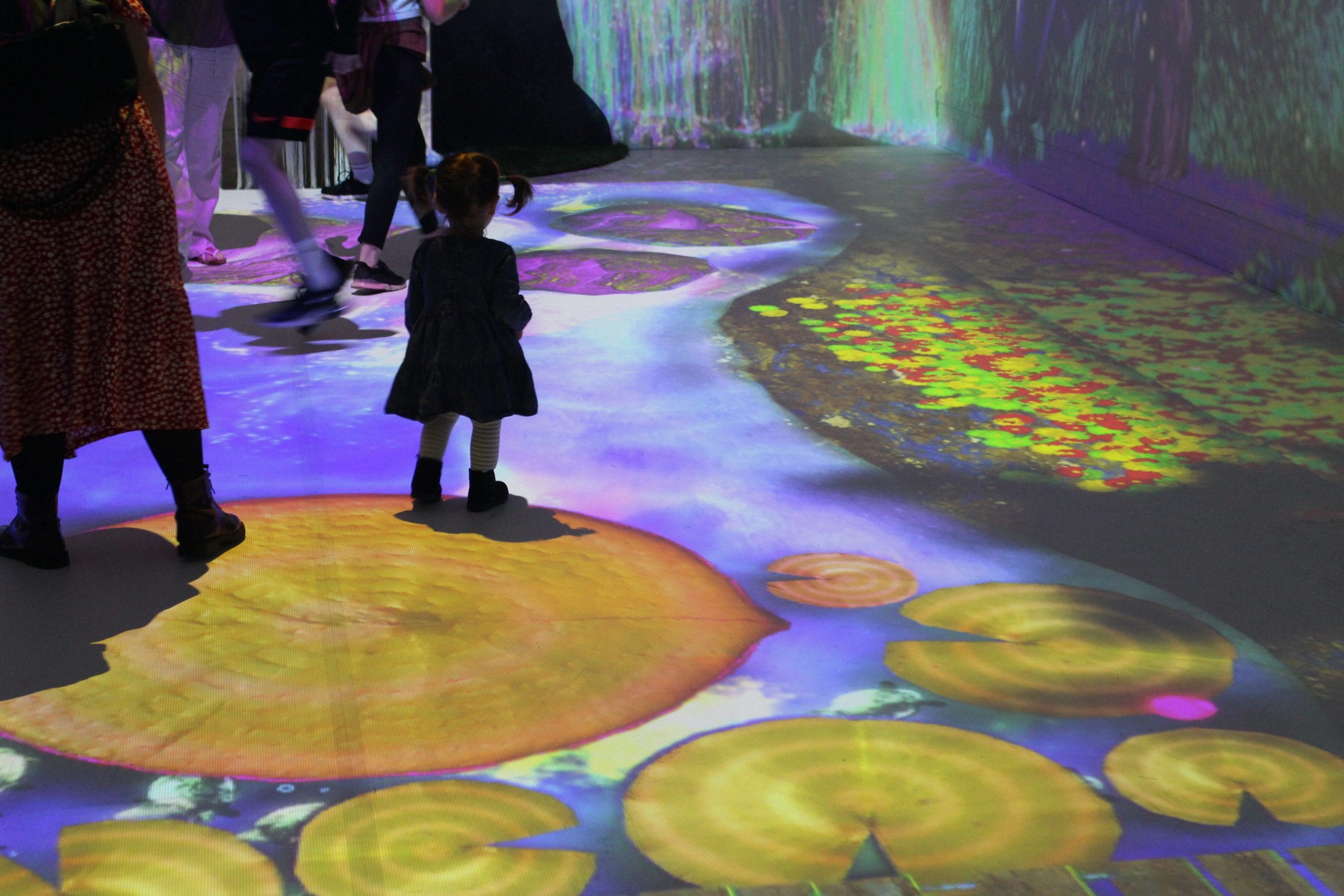 A small girl enjoys projected lily pads on gallery floor