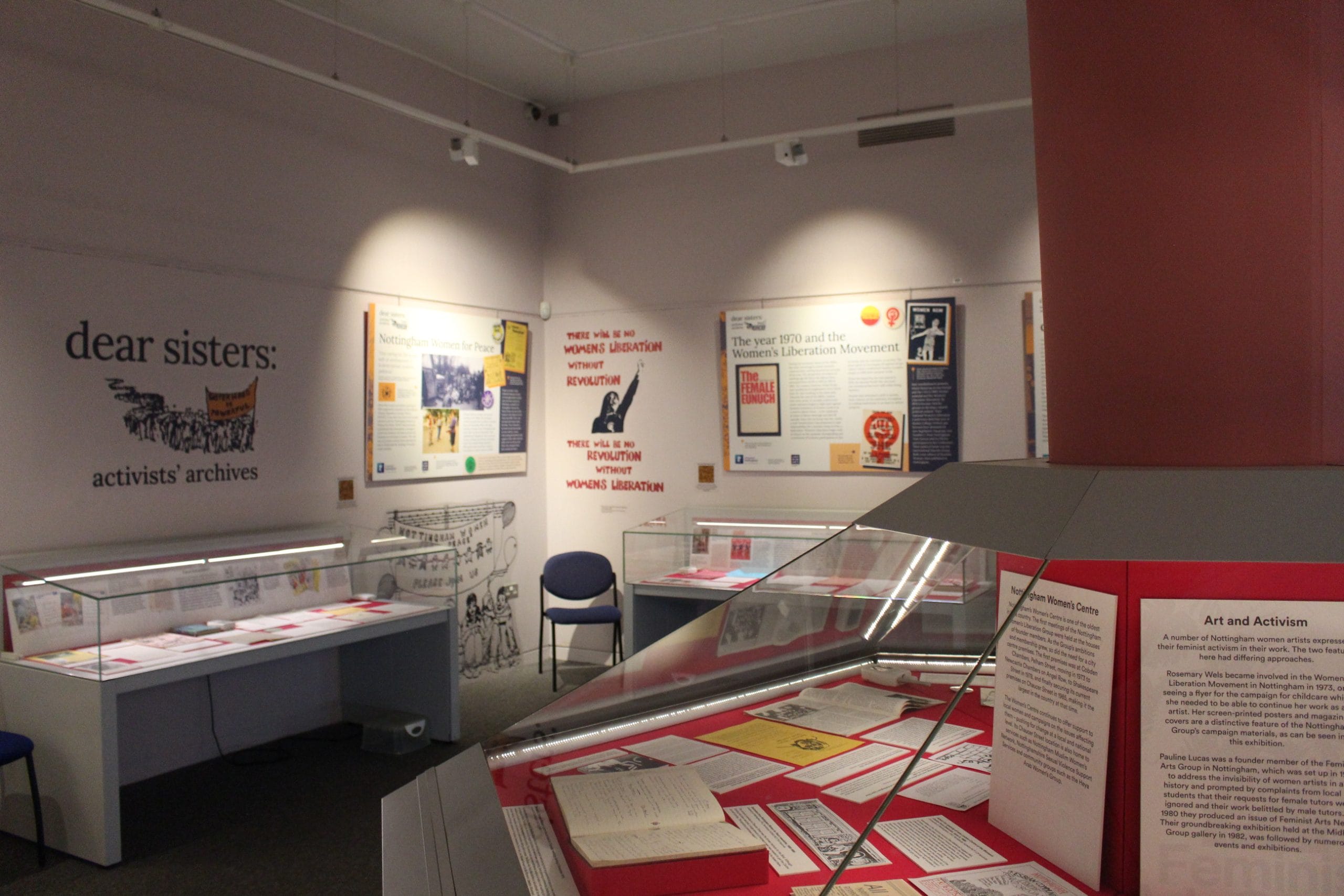 A photo of part of the Dear Sister exhibition with glass display cases and feminist slogans on the walls