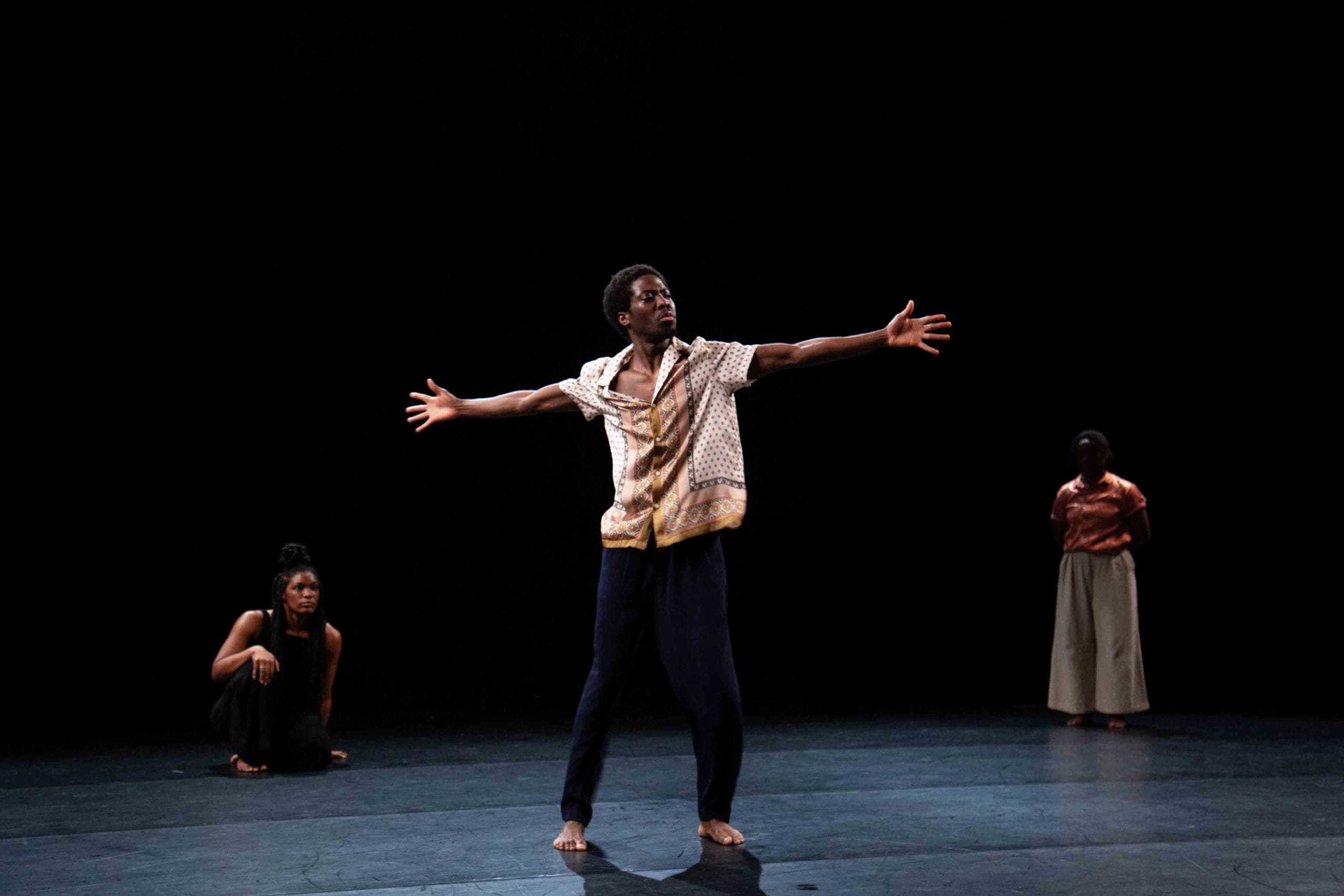 A dancer raises his arms out as people crouch next to him