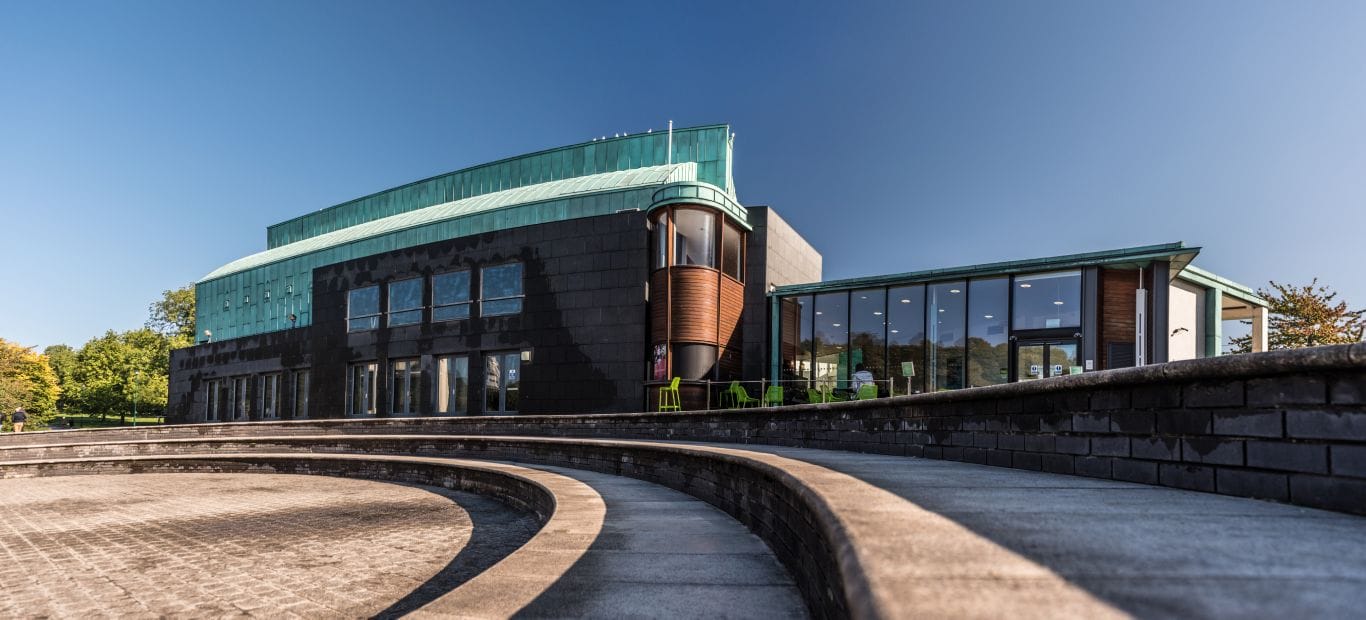 A building with a green roof and large windows sat next to a lake
