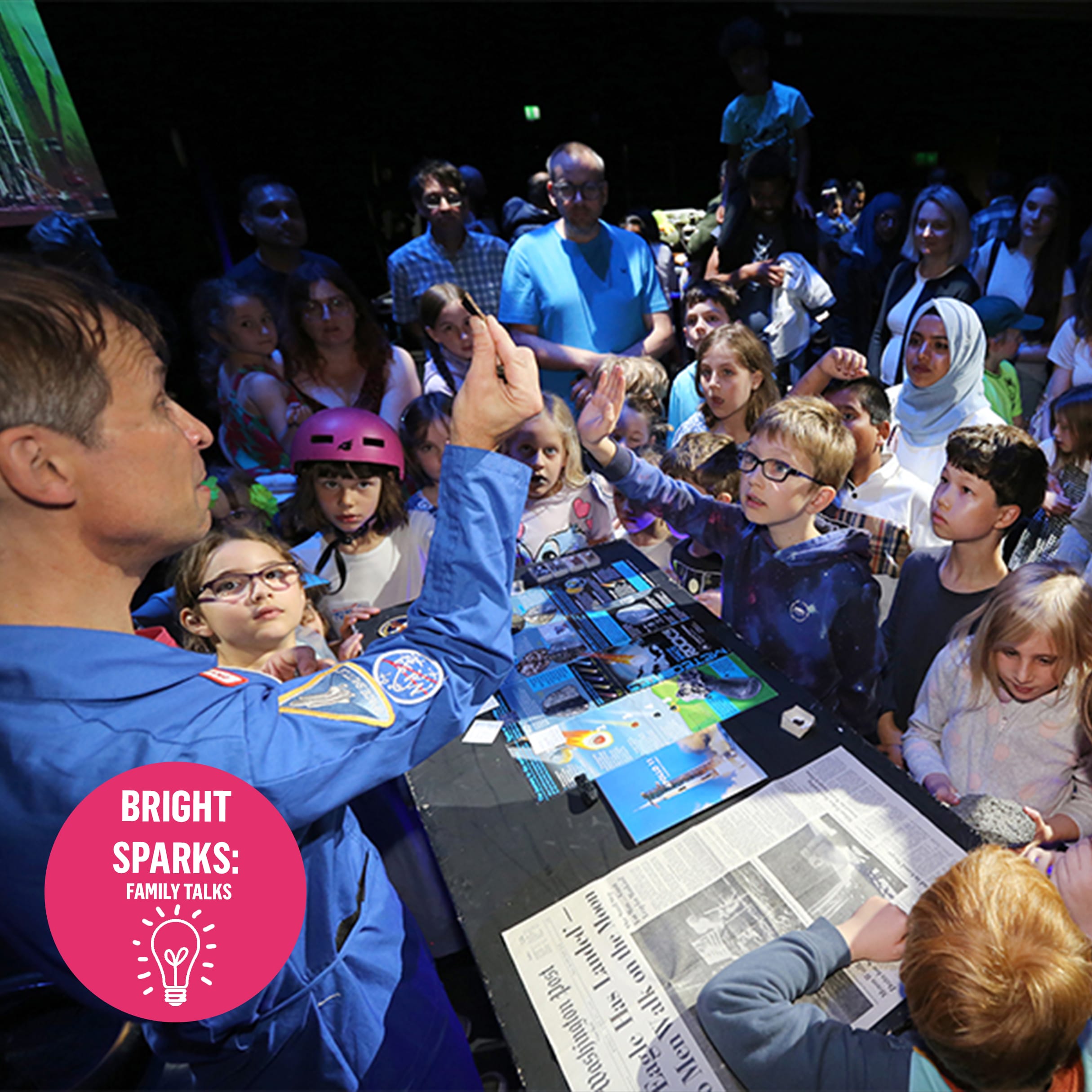 A man in a space suit shows a group of kids a small piece of space rock