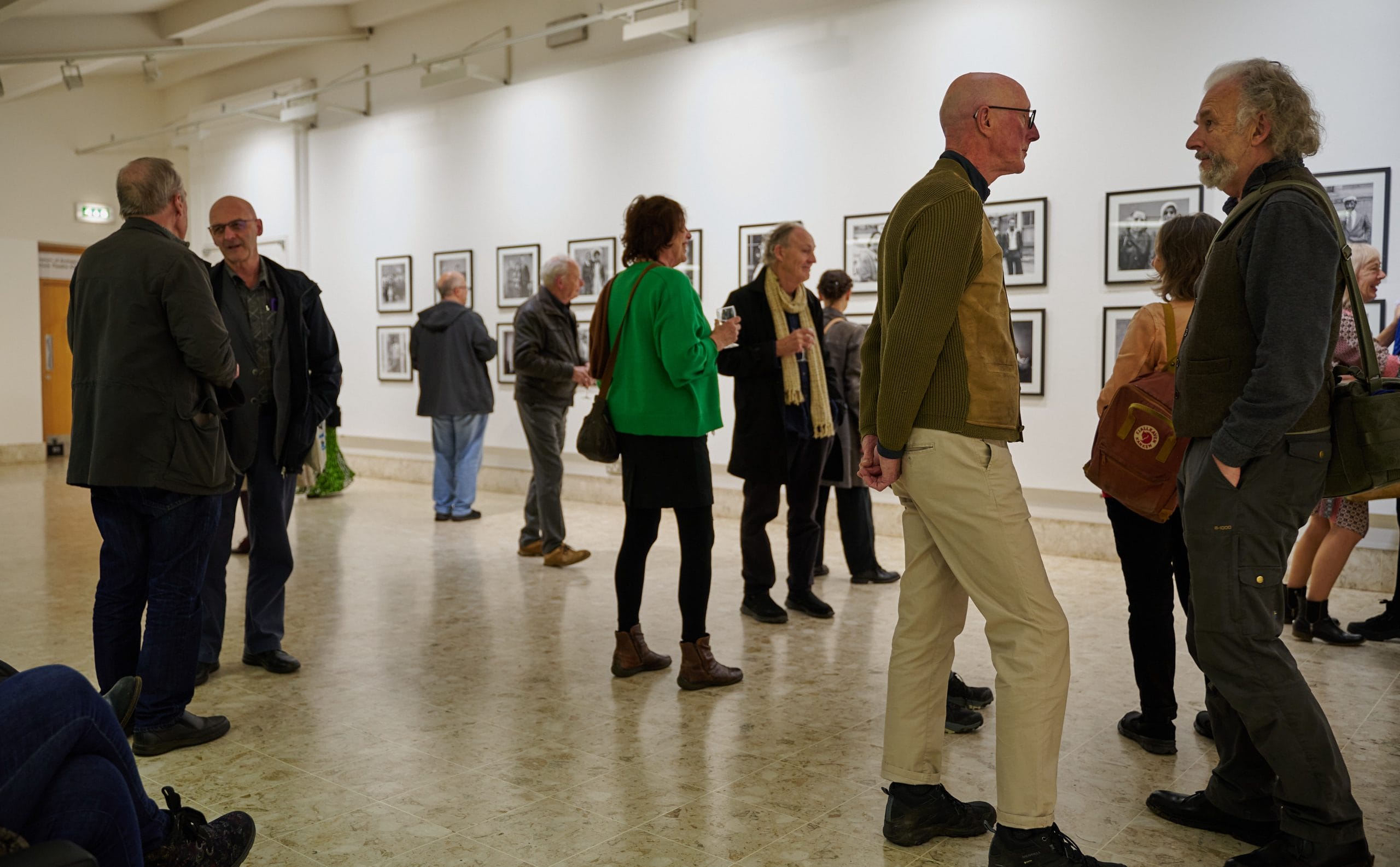 People enjoying artworks and chatting in a bright, white art gallery.