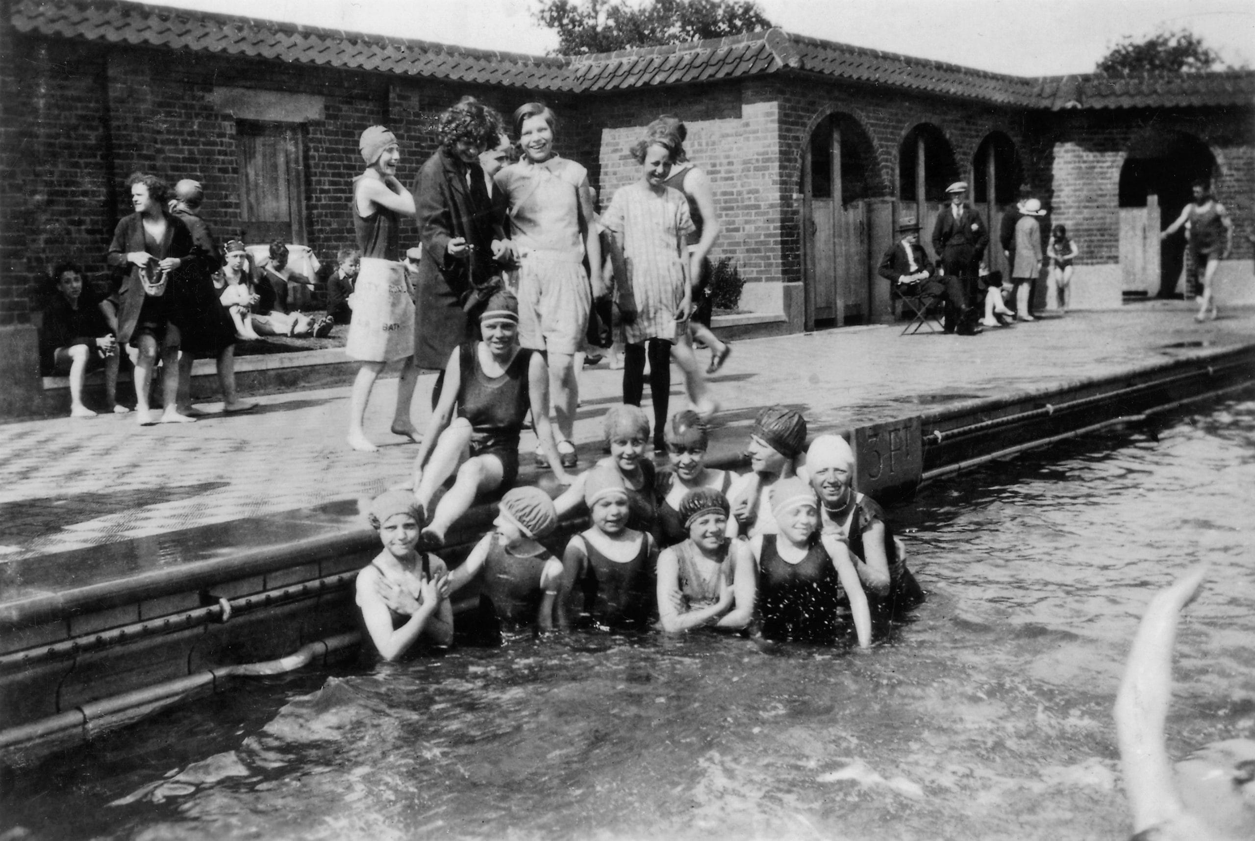 A black and white photo of a group of women swimming in an outdoor pool