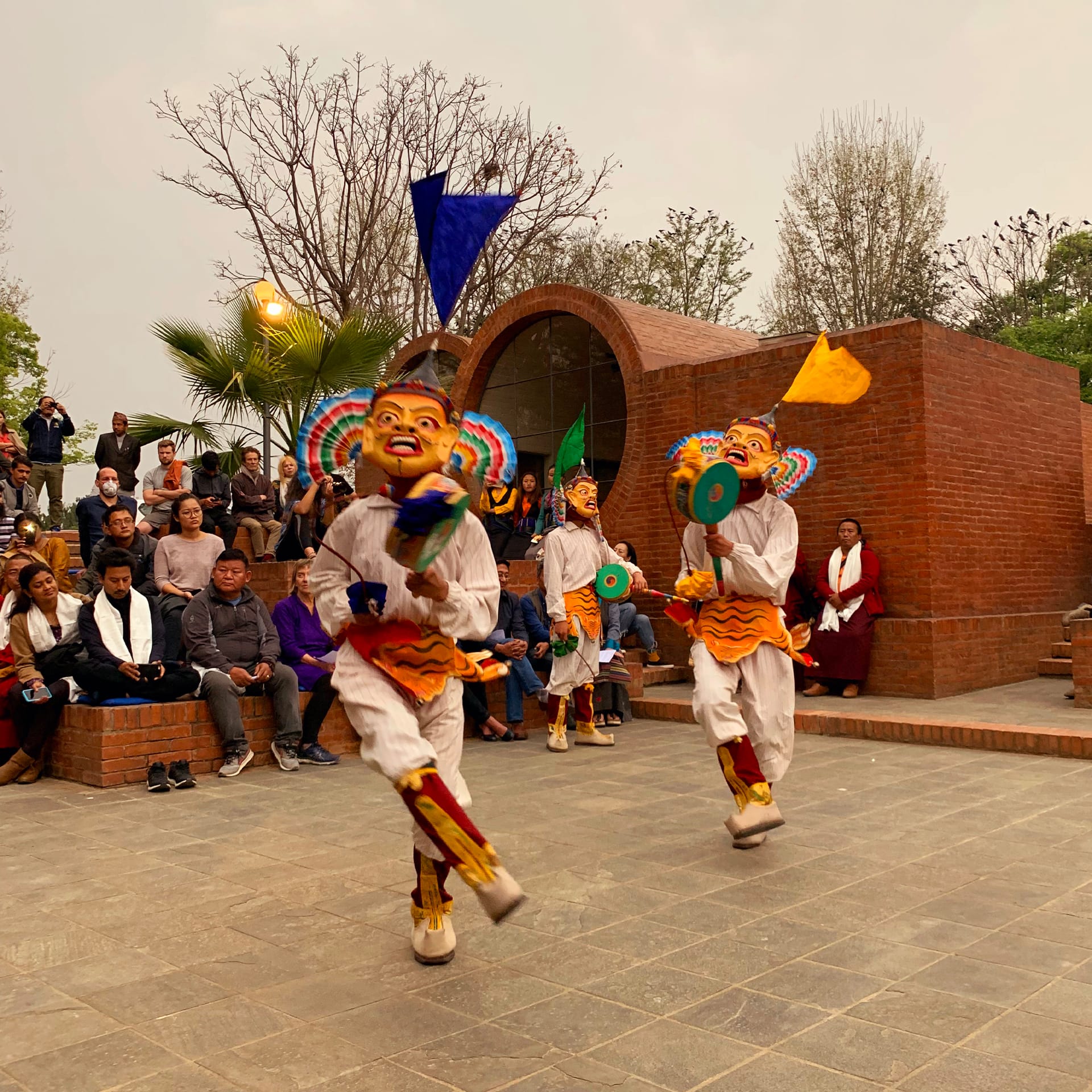 People dressed in white with yellow masks and drums dancing on pavement