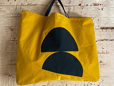 A bright yellow bag with blue semi circles, against a brick wall