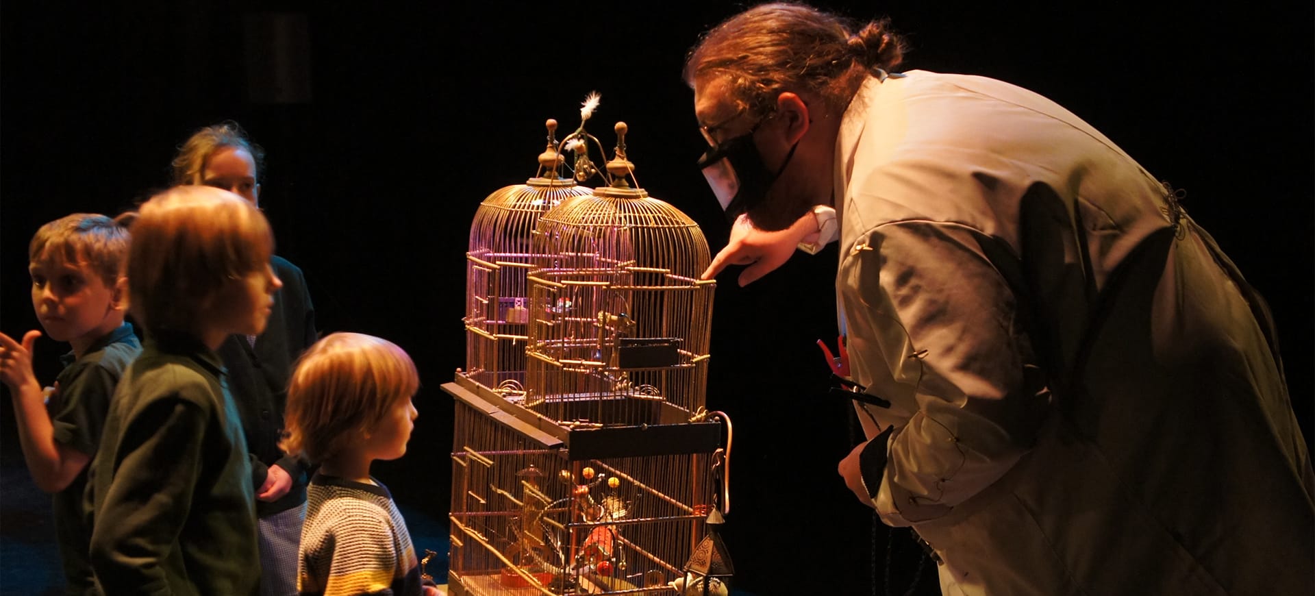 A man in a lab coat shows children robots in a cage for Thimgamabobas
