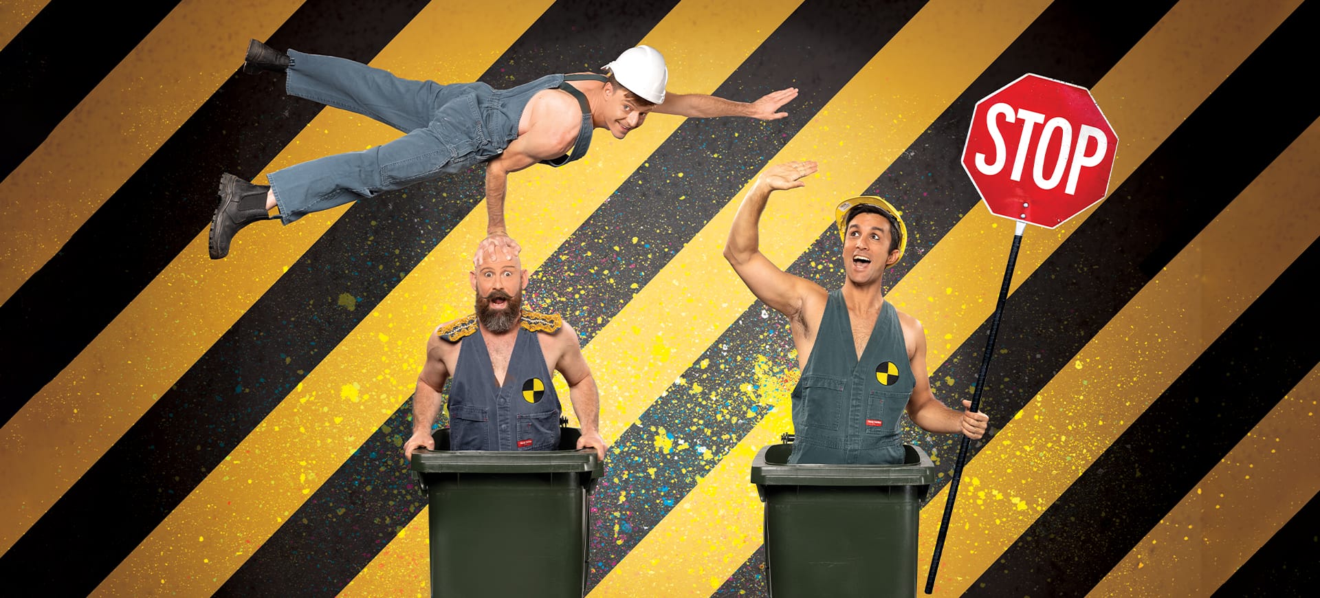 Two men in overalls stand in wheelie bins whilst another balances on their head.