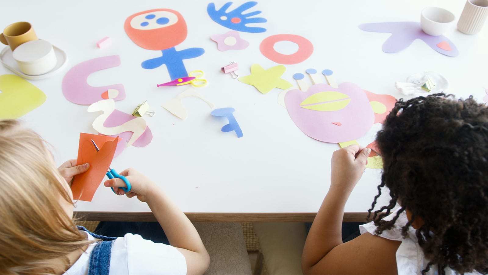 Two young girls cut out paper shapes