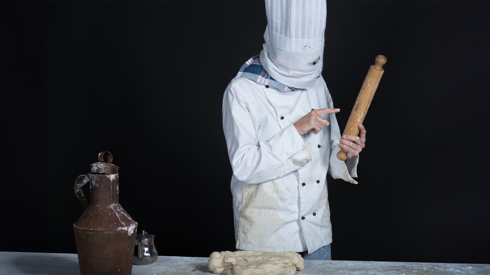 A person dressed as a chef points accusingly at a rolling pin
