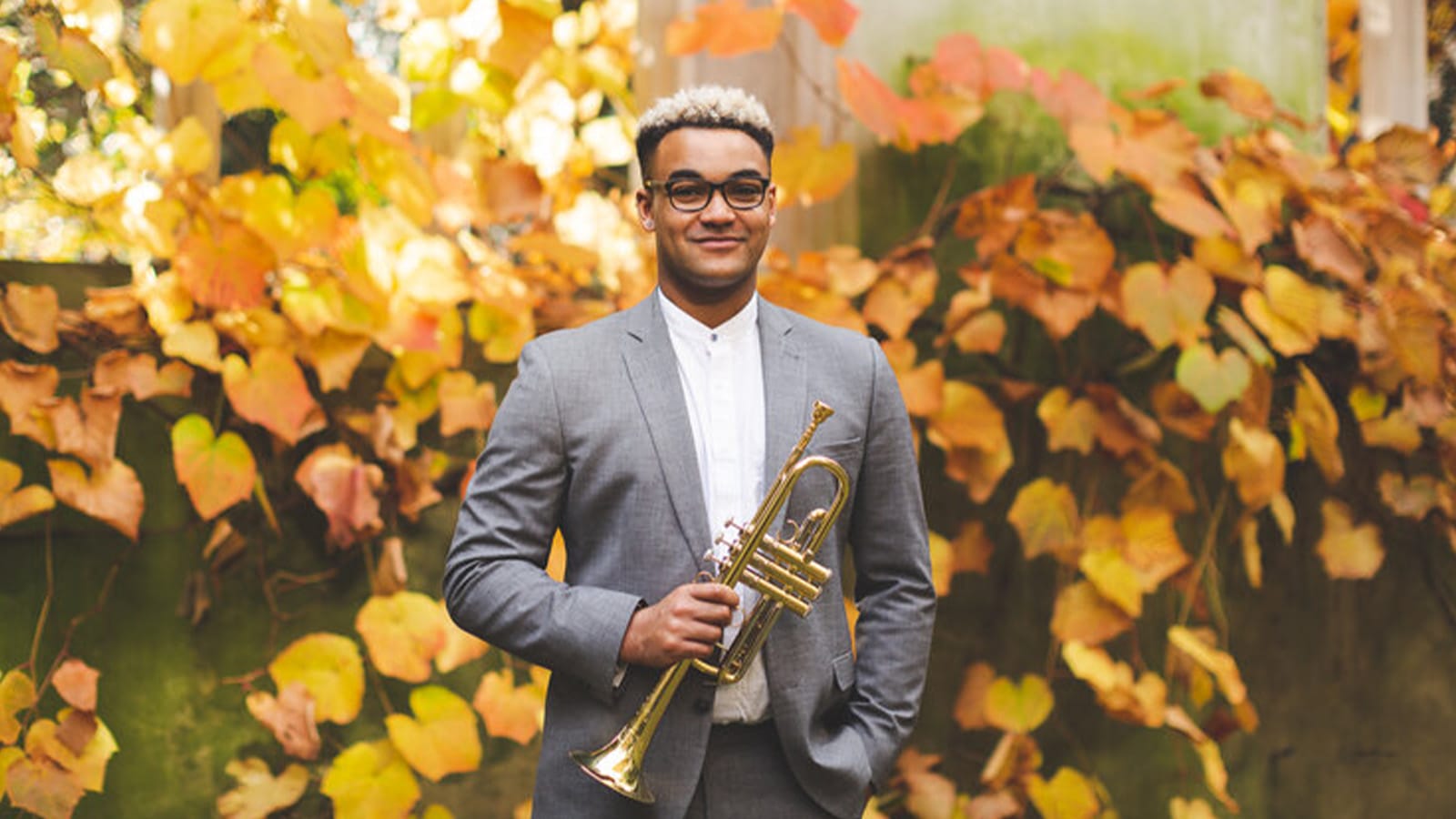 A man stands in a grey suit holding a trumpet