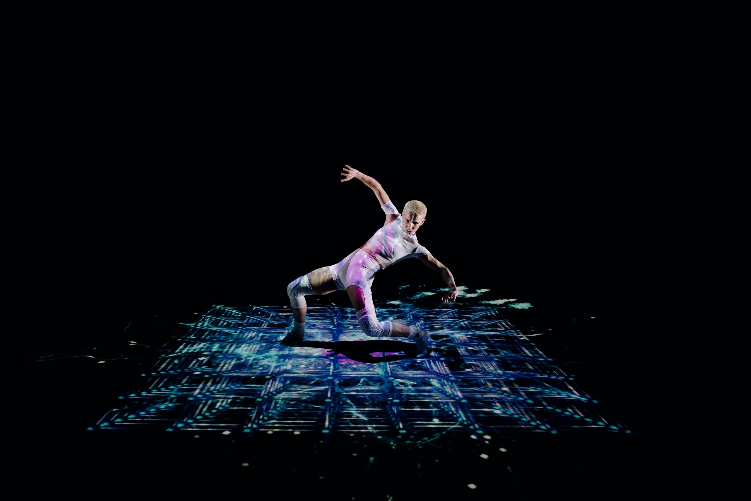 A dancer on stage surrounded by light projections