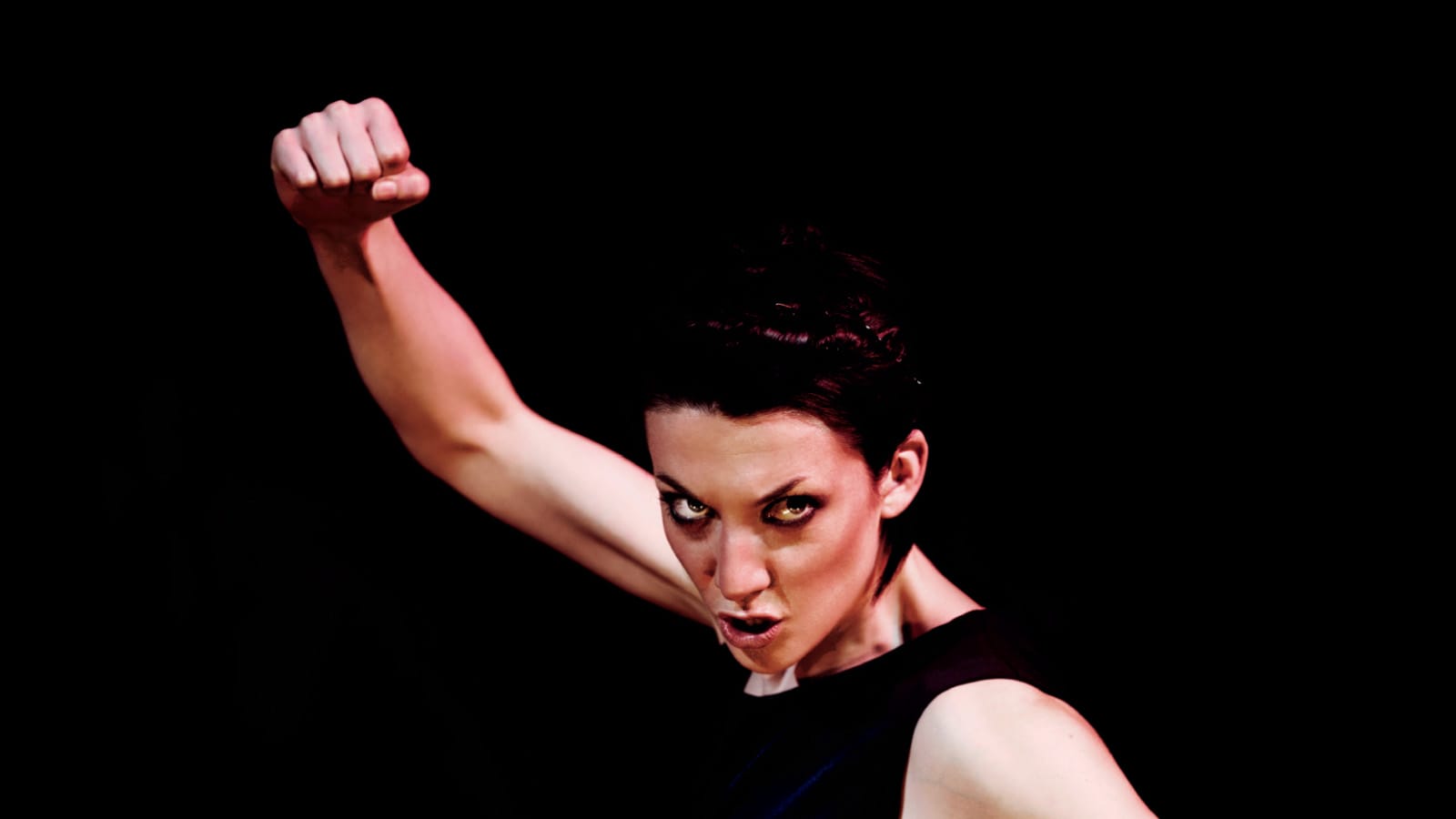 A woman wearing all black holding her fist up aggressively