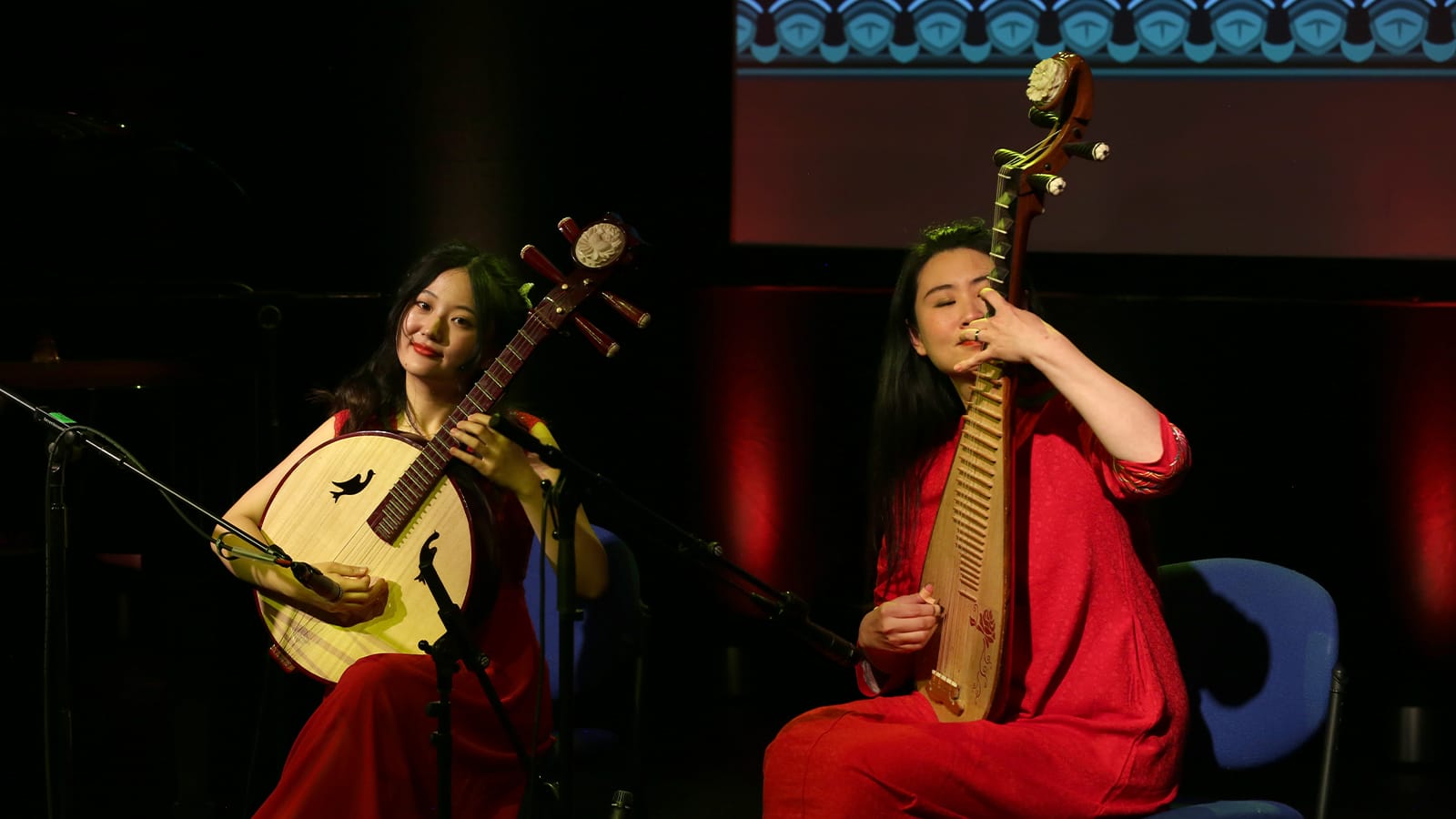 Two women in red dresses play traditional string instruments
