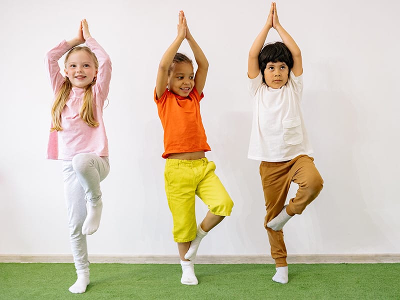 Three children put their feet on their legs and hands above their heads in a martial arts pose