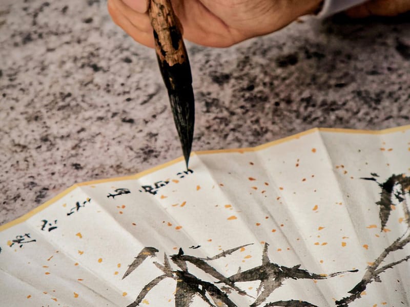 A fan being painting with Chinese characters