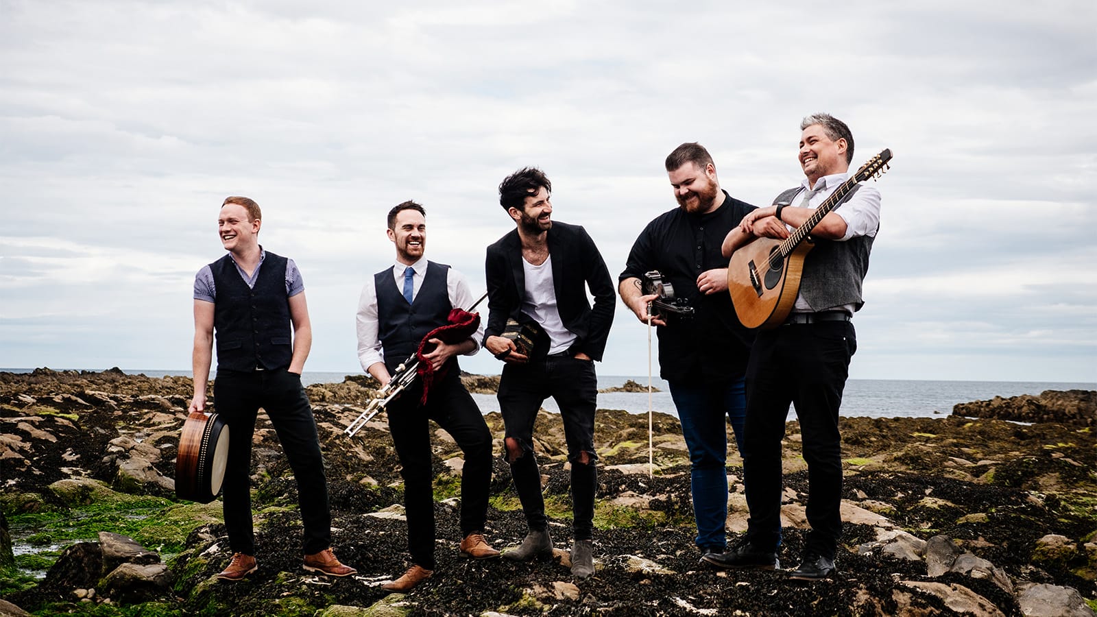 five men stand on a mountain holding various instruments