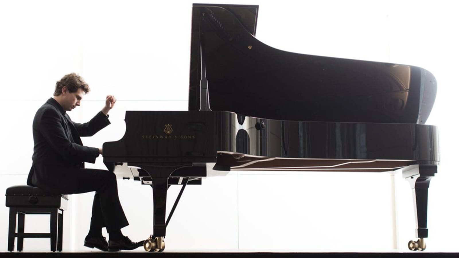 A man in a black suit plays a grand piano