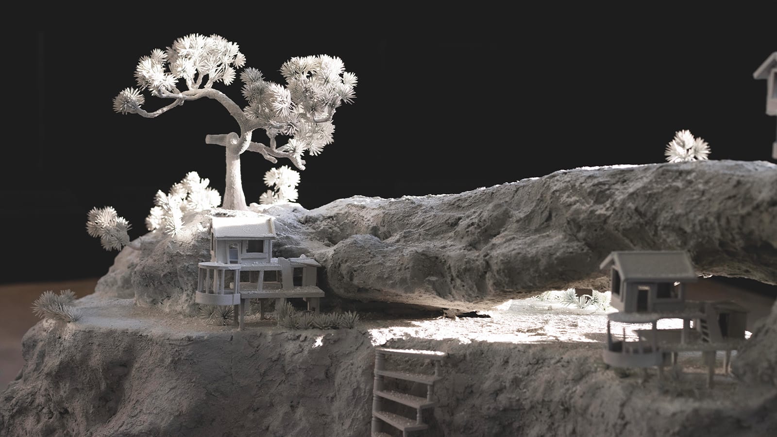 A grey sculpture of a tree and a house on a desolate rock landscape