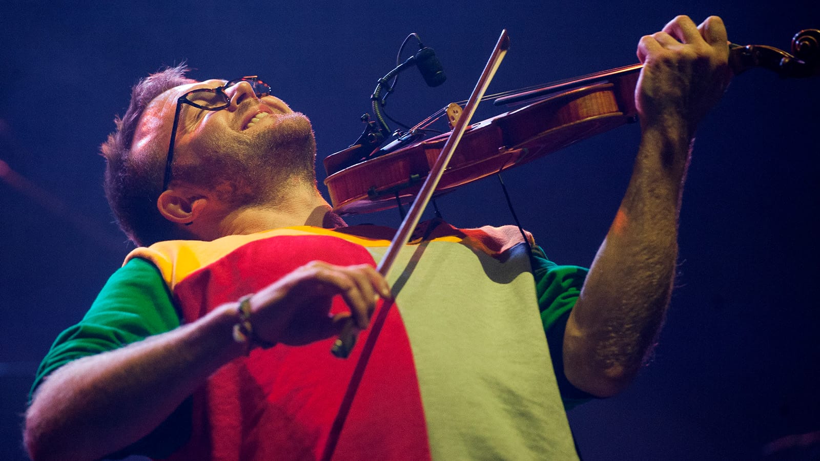 A man in a red and yellow t shirt plays the fiddle