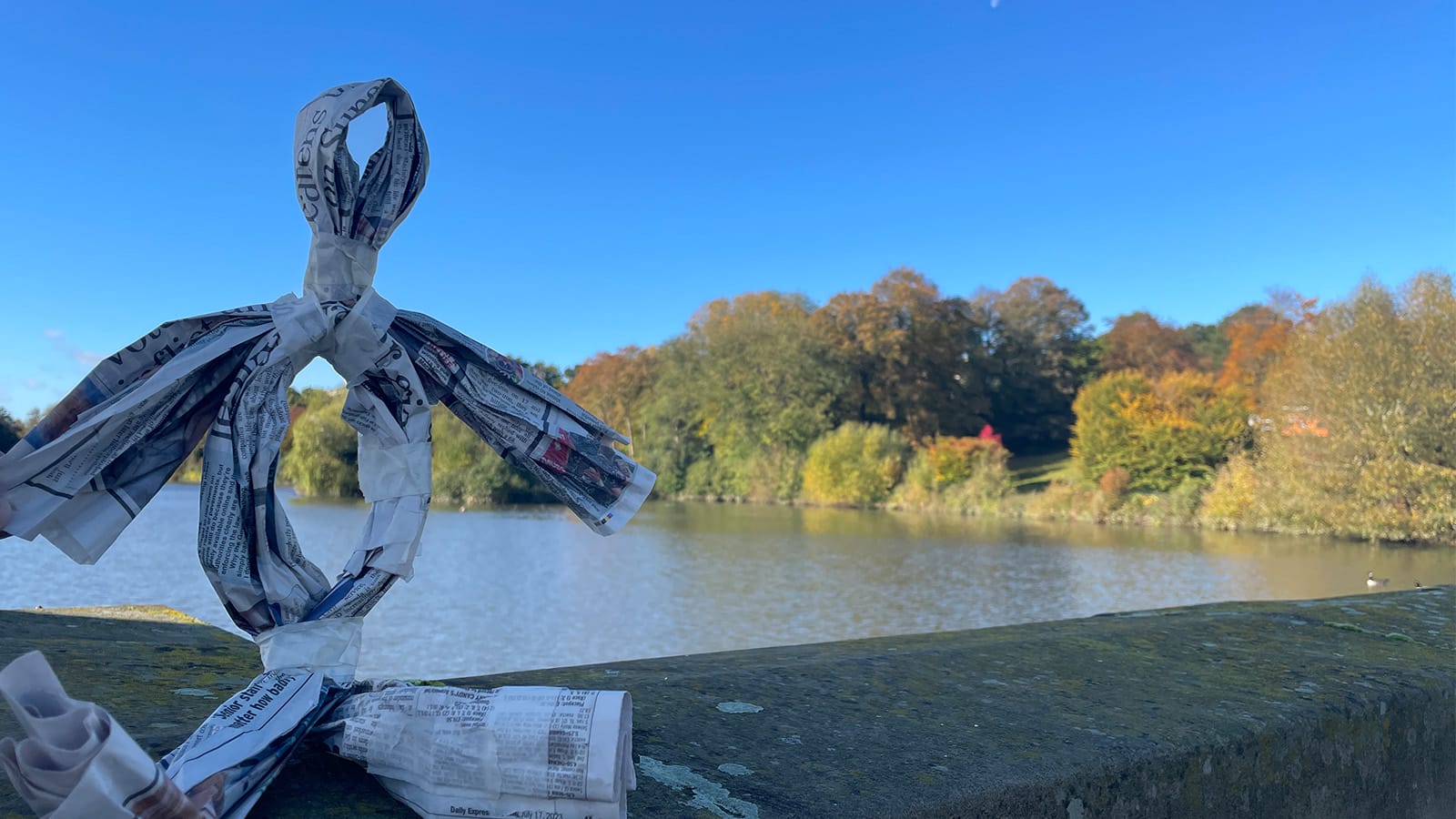 A puppet made of paper sitting on a wall by a lake