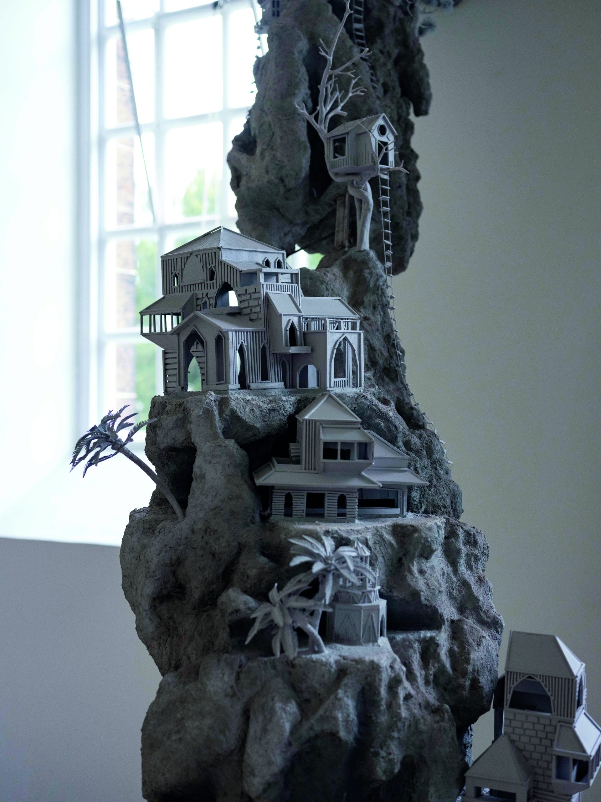 A grey towering sculpture with tiny grey houses and trees