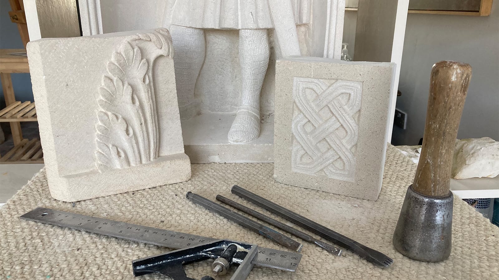 A selection of stone carving tools in front of stone carved with ornate patterns