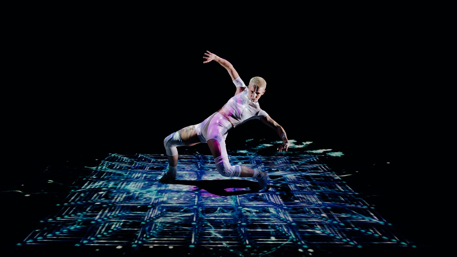 A woman bends backwards in a dance, surrounded by pink projections