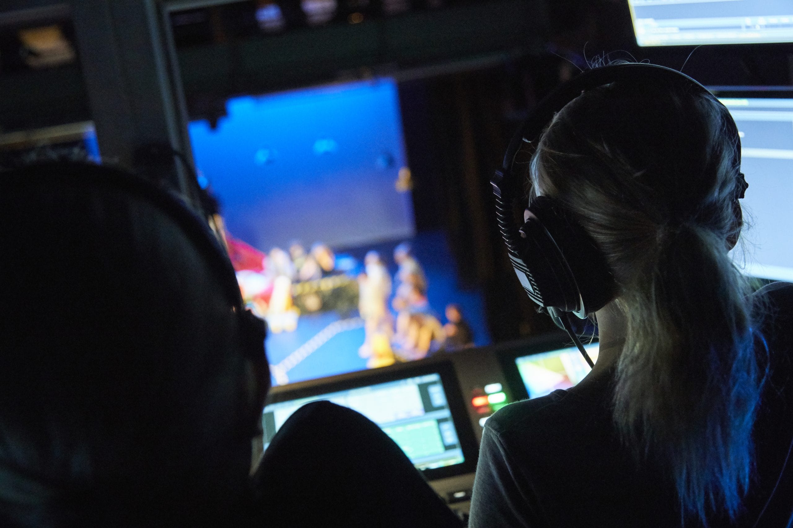 The backs of two people's heads wearing headphones and operating the tech for a theatre show