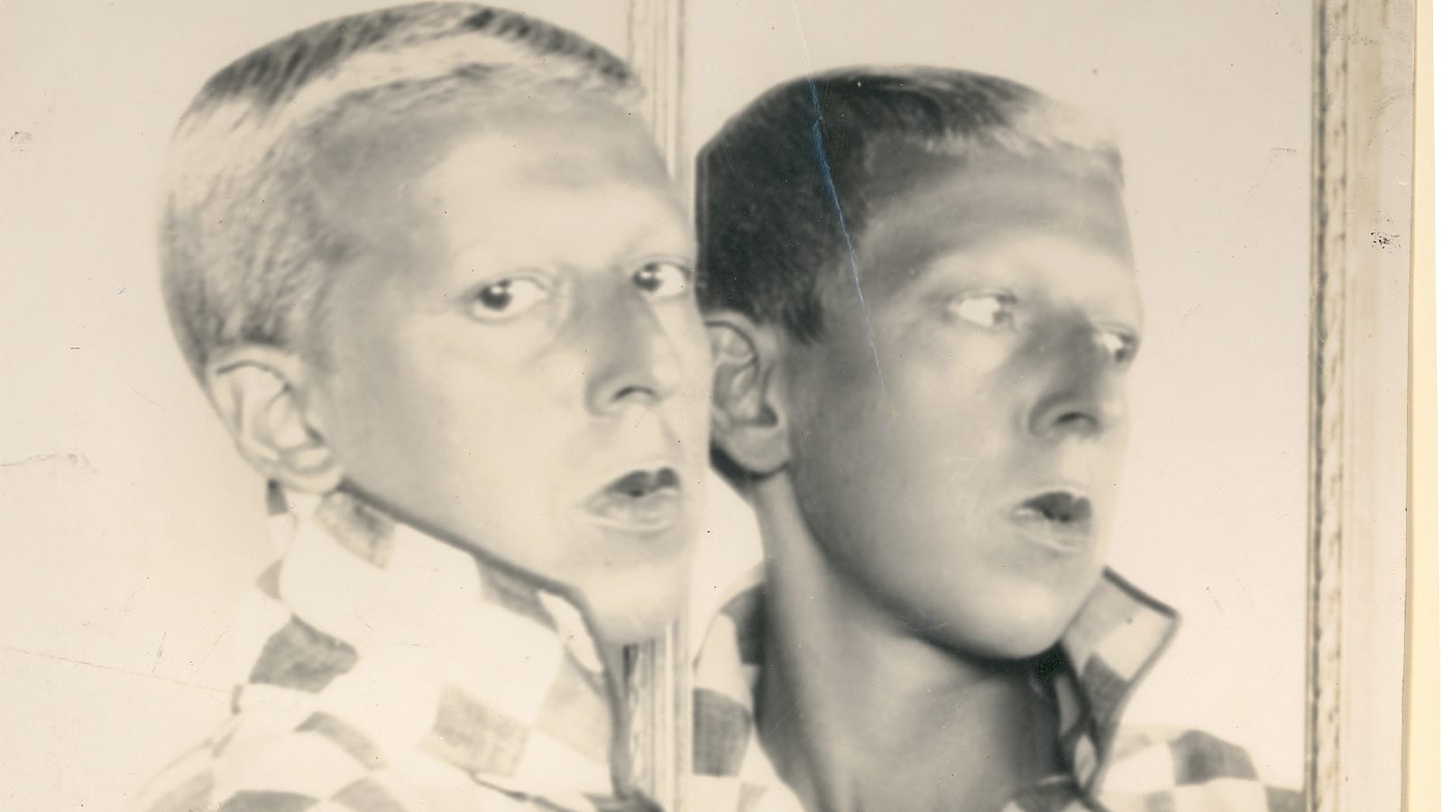 A black and white photo of a man looking in a mirror
