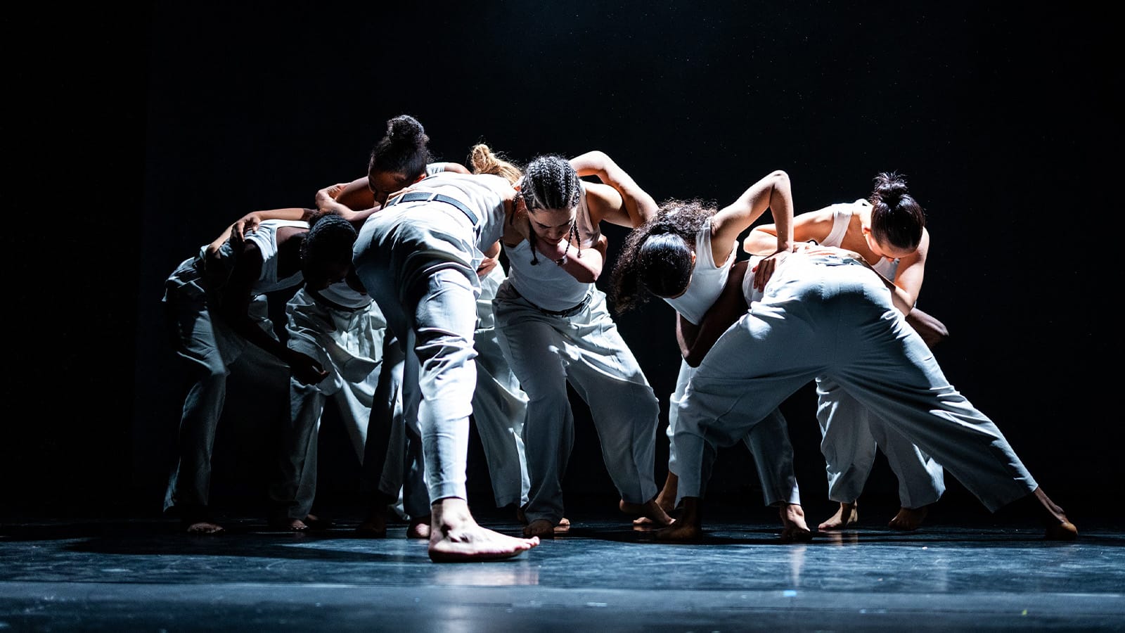 A group of dancers wearing white group their heads and arms together in a circle