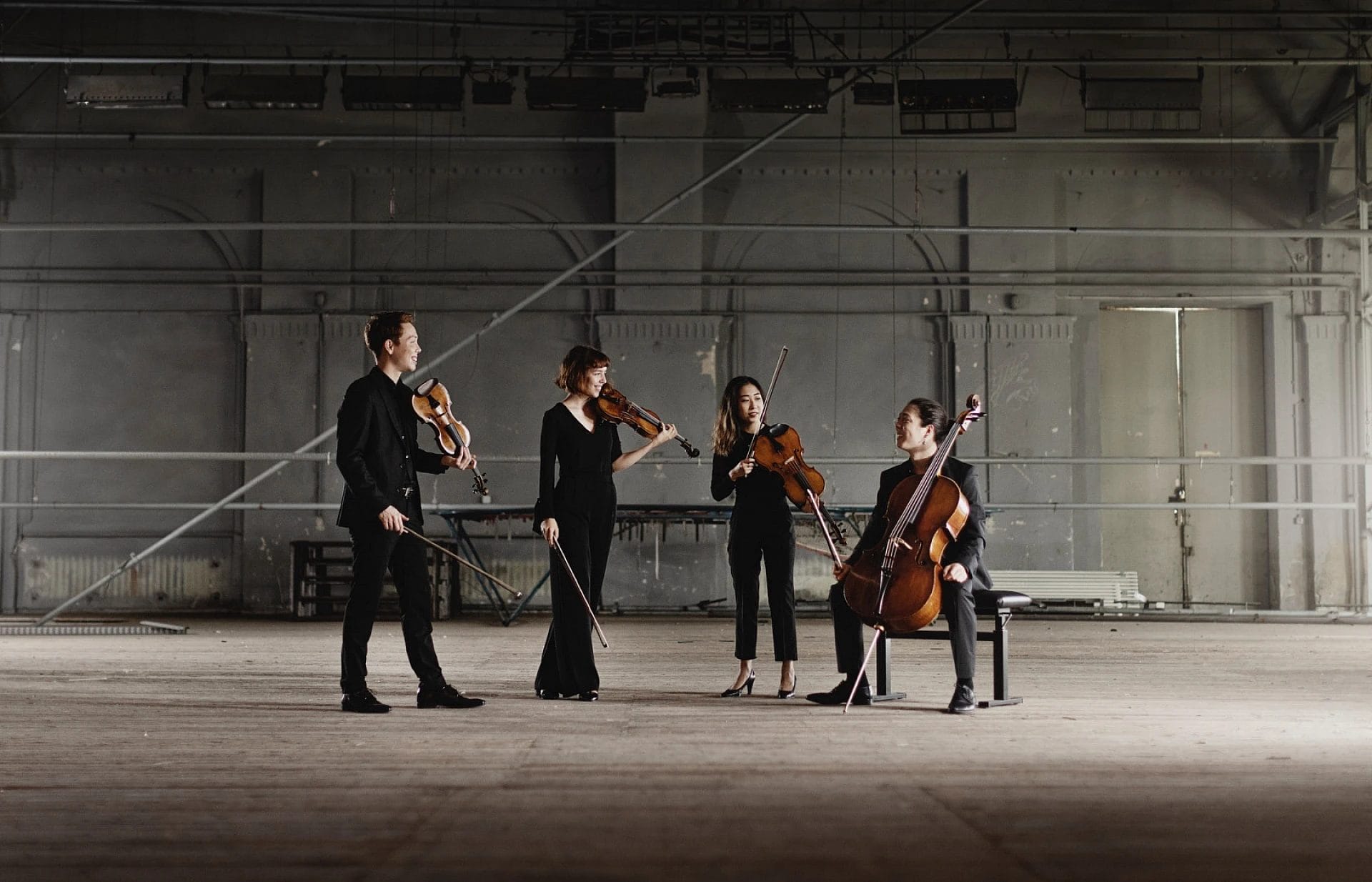 A string quartet hold up their instruments; a cello, two violins and a viola