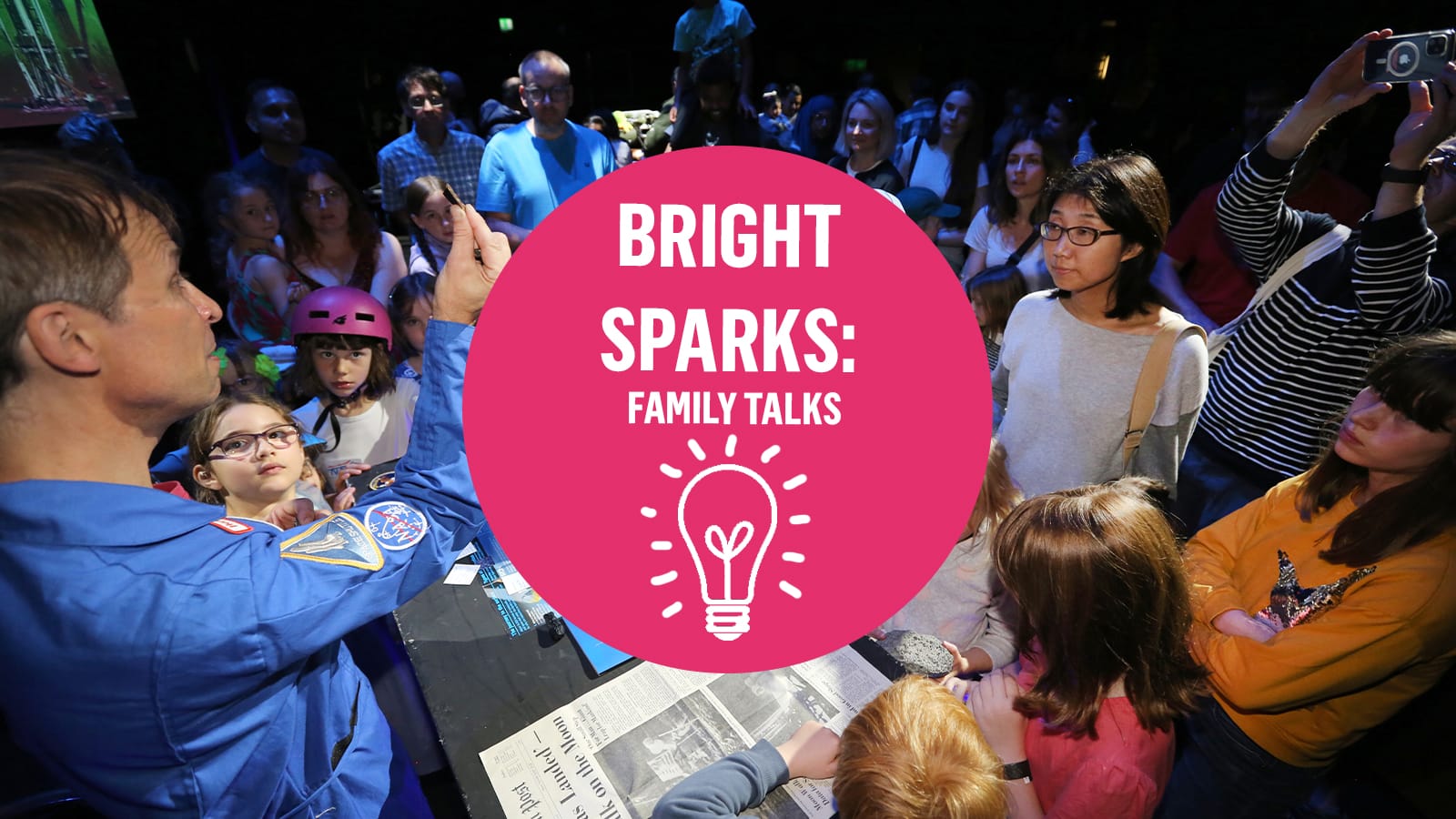 A man in a space suit shows a group of kids a small piece of space rock