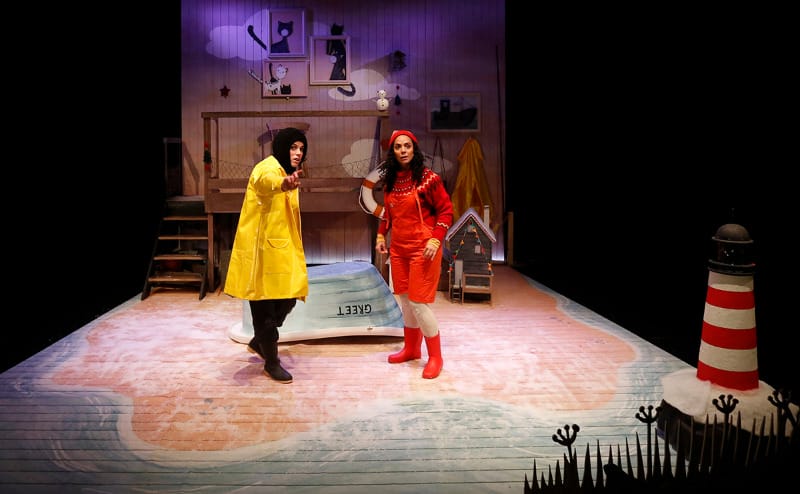 A person in a yellow coat and one in a red suit and wellies stand on a sandy beach