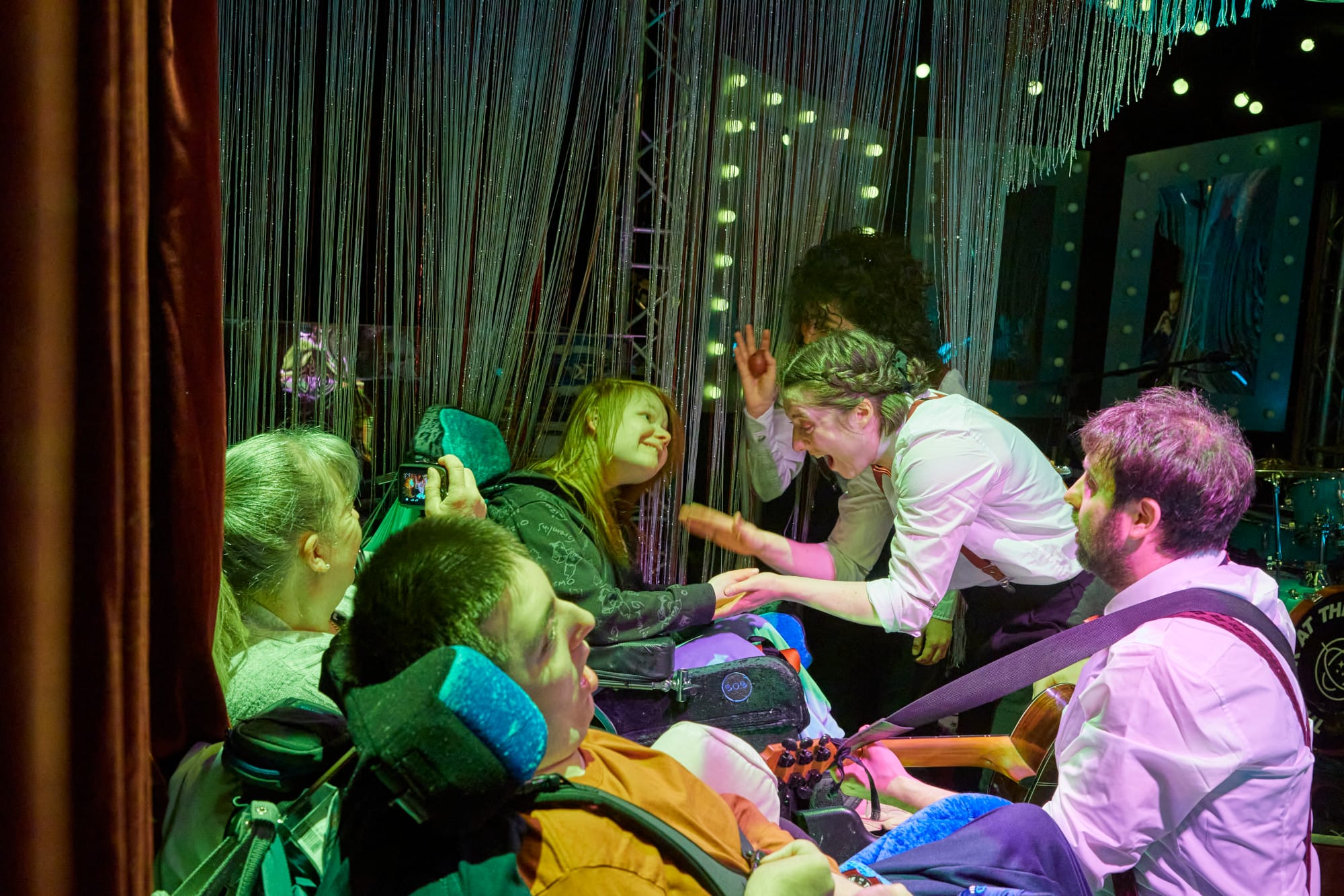 Two young people in wheelchairs engaging with actors from Frozen Light theatre company.