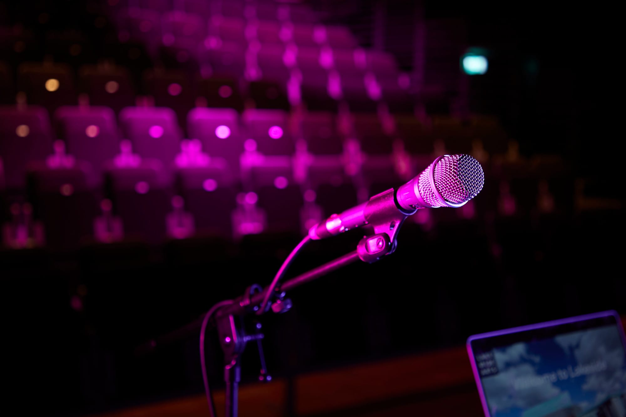 Close up of microphone on stage. with audience seating in the background.