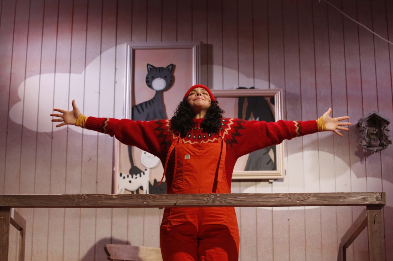 A woman in a red jumpsuit stretches in front of a picture of a cat