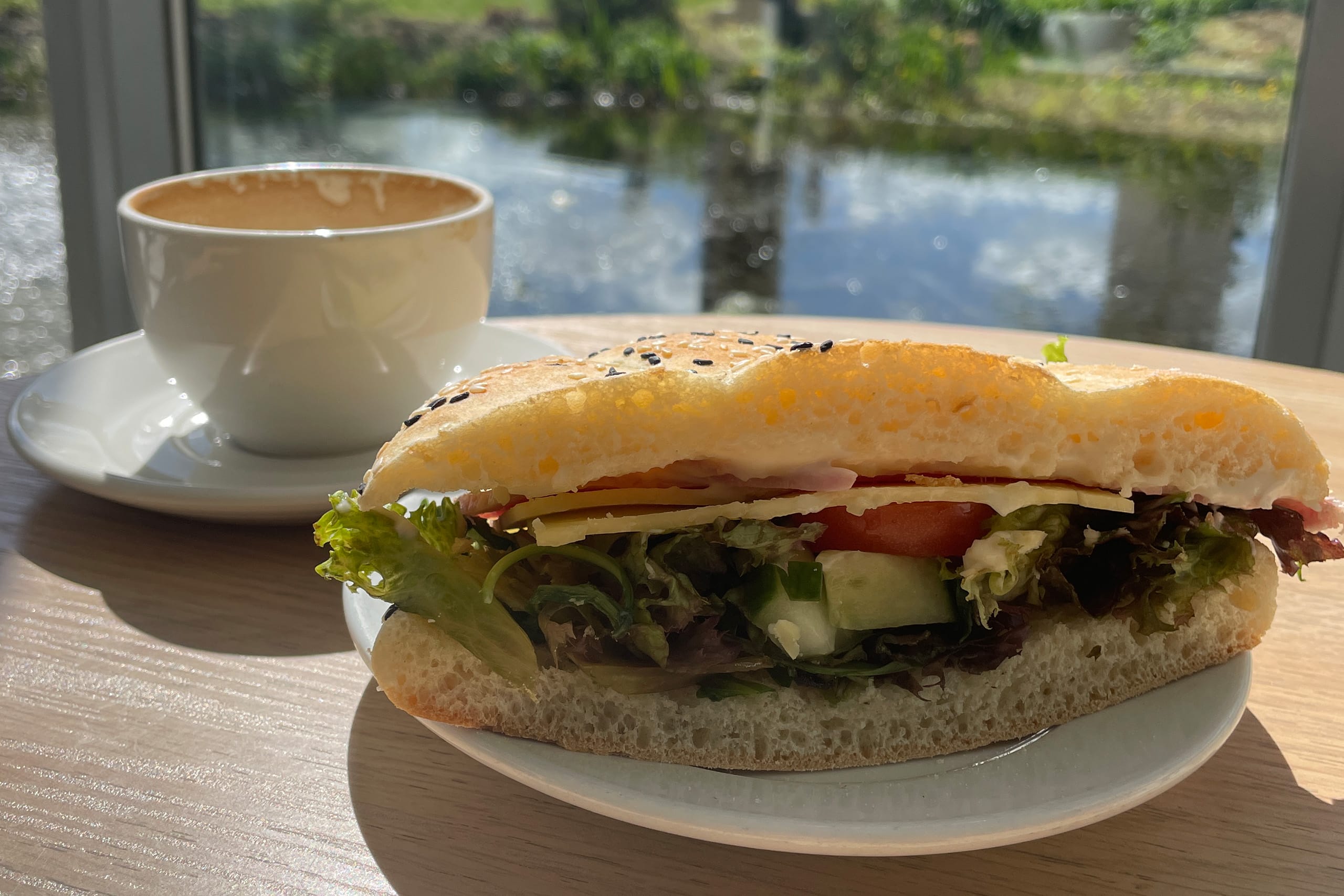 A plated cheese and salad sandwich sits on a table with a water feature in the background.