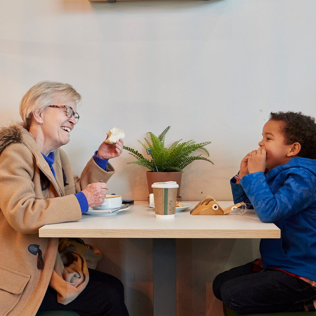 A child sits opposite a lady, enjoying food and drink in a café