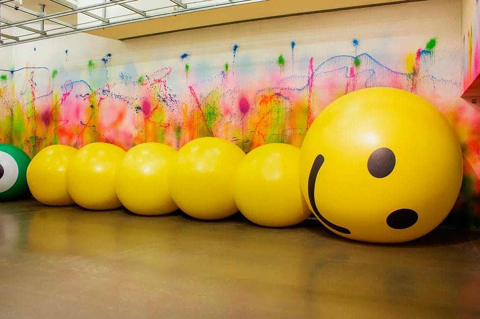 a photo of a giant yellow inflatable worm with a smiley face in a gallery space