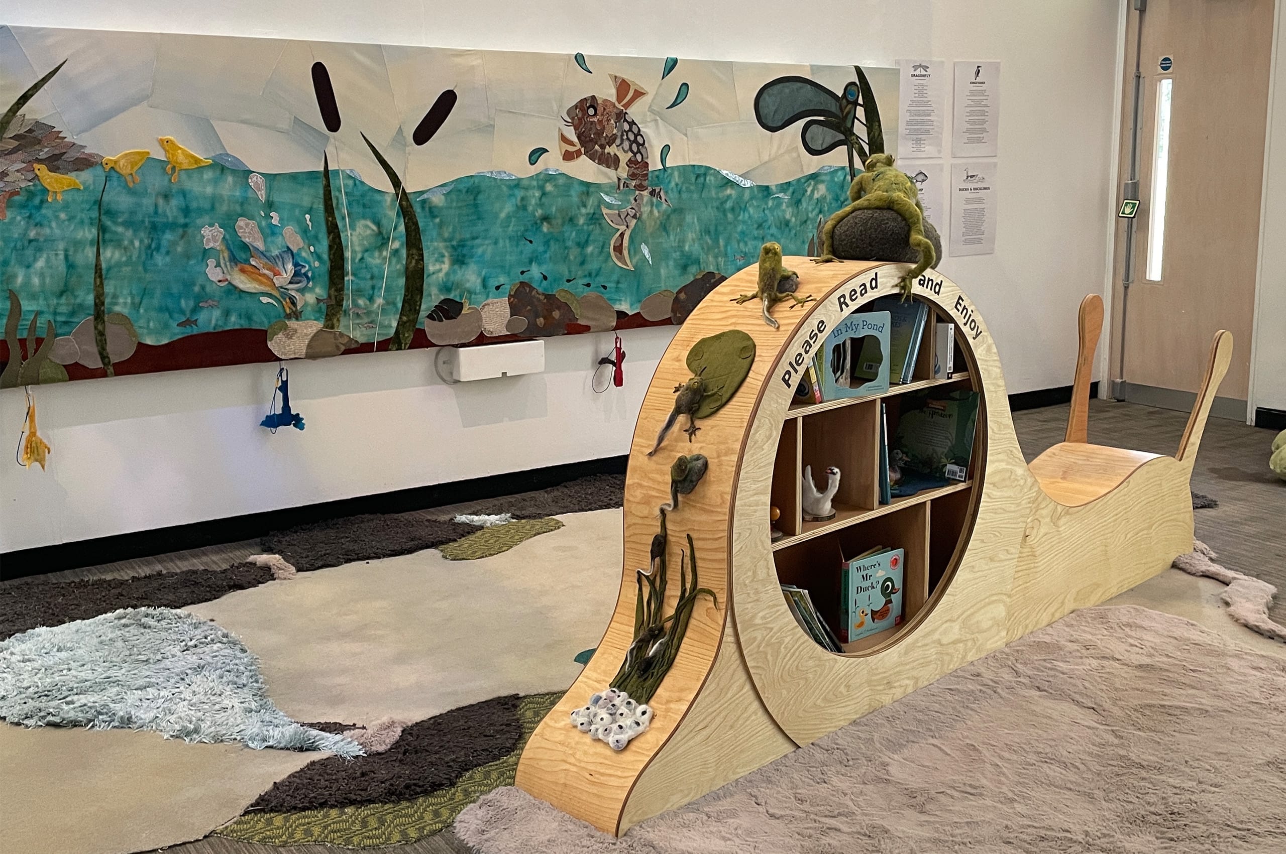 A gallery space with a reading snail in the foreground and a collage underwater scene on the wall.