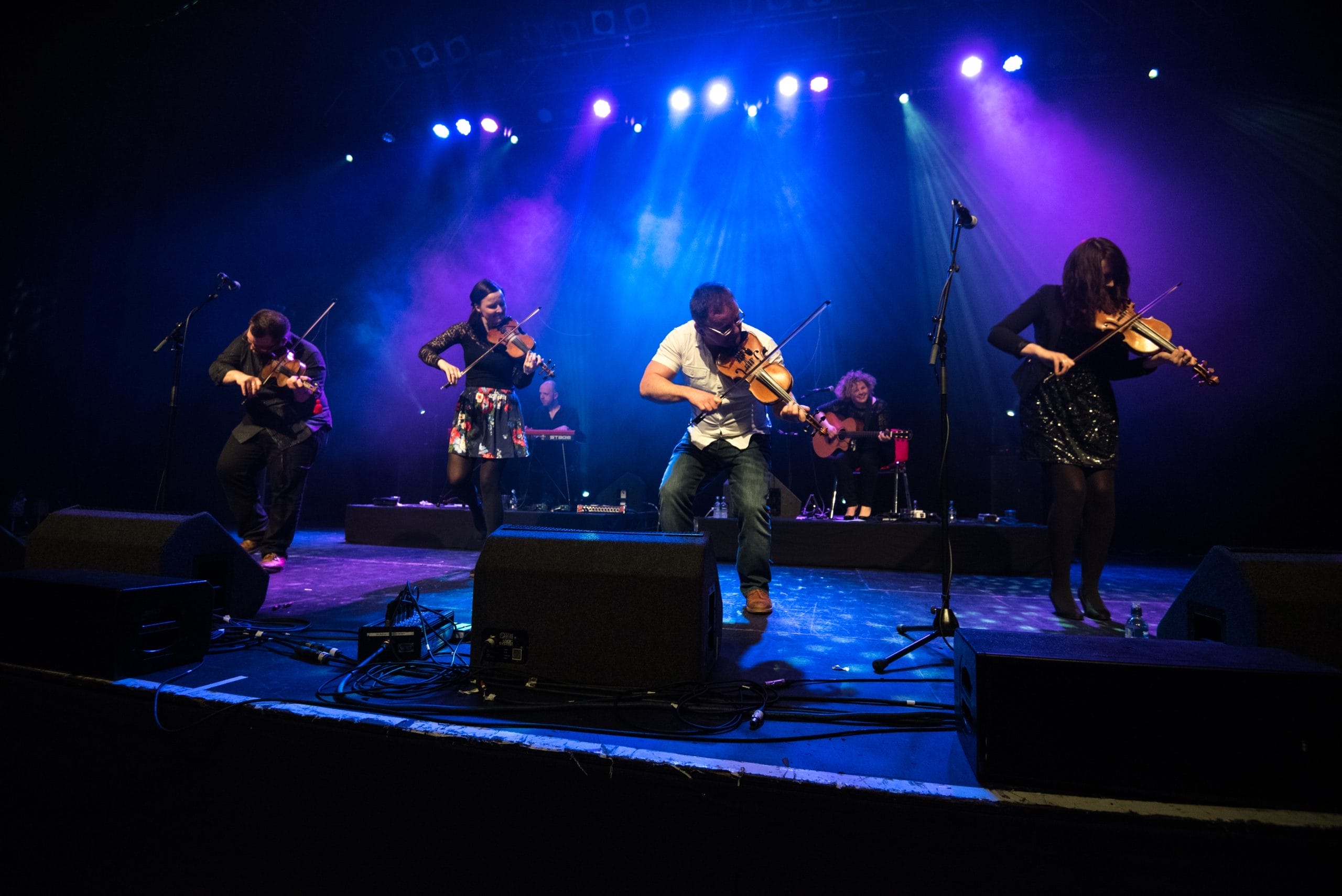 Four artists playing fiddles on a stage