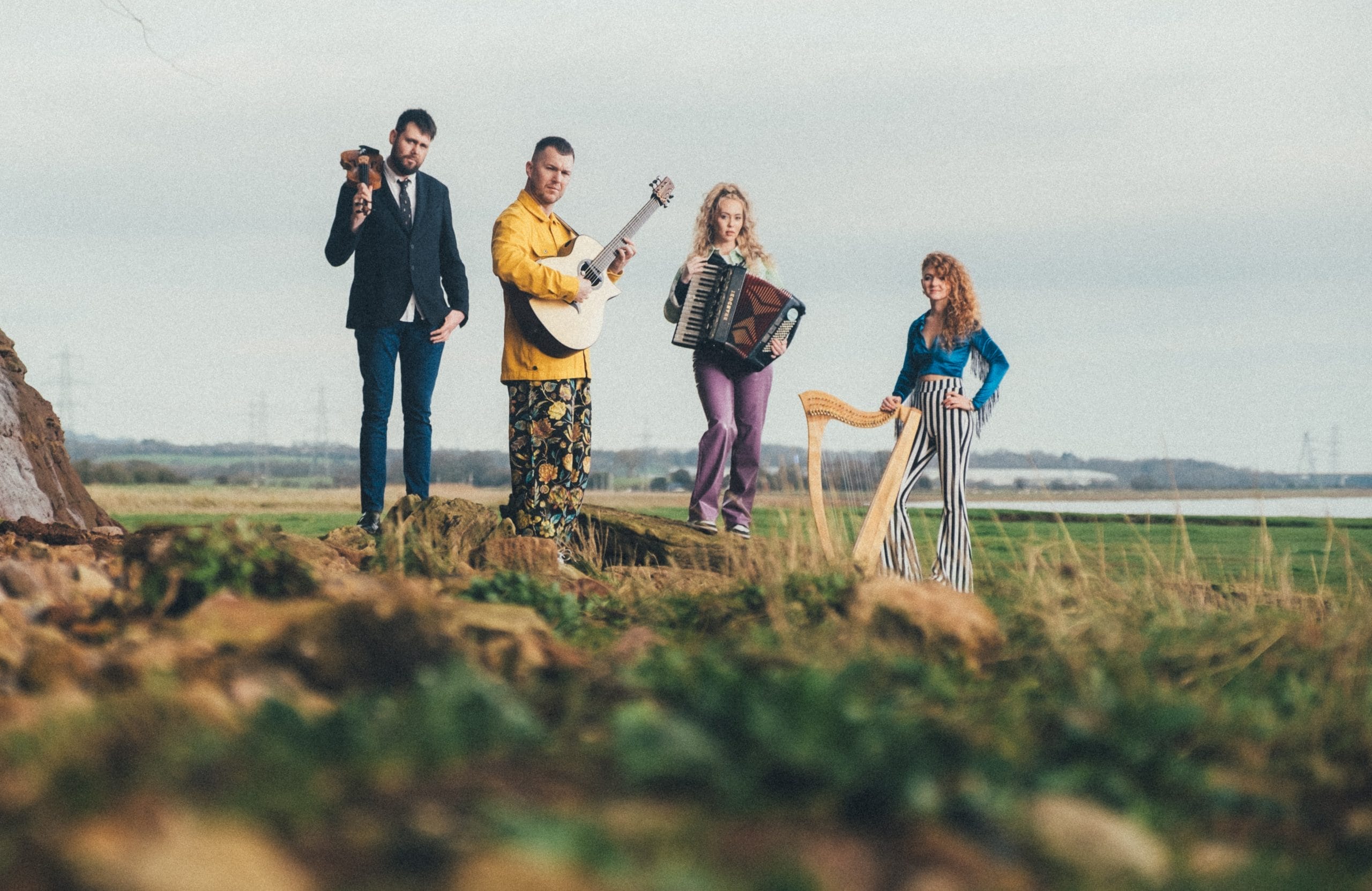 Two men and two women all holding various instruments standing in open field .