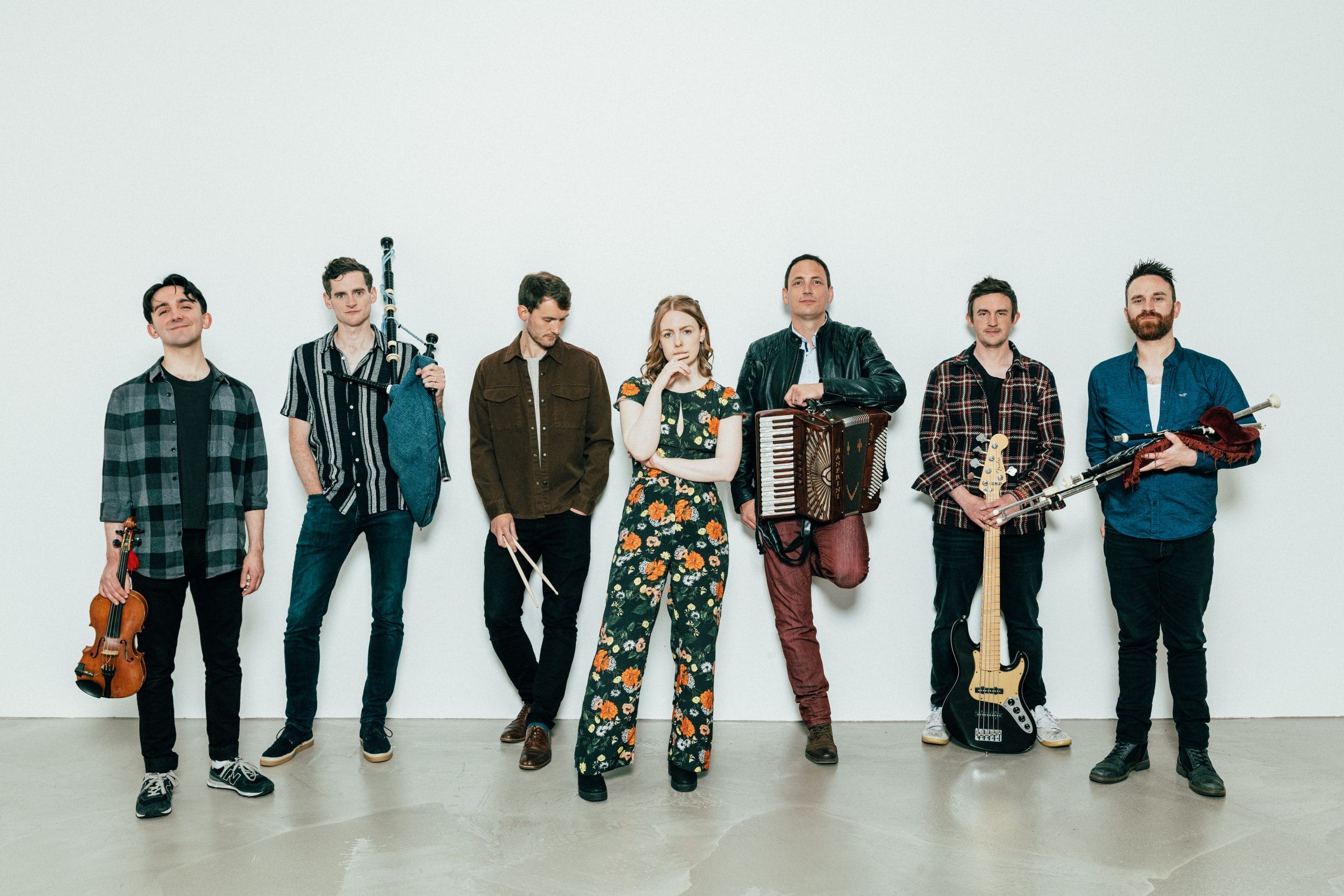 group of 7 people with all men holding instruments standing infront of light grey backdrop